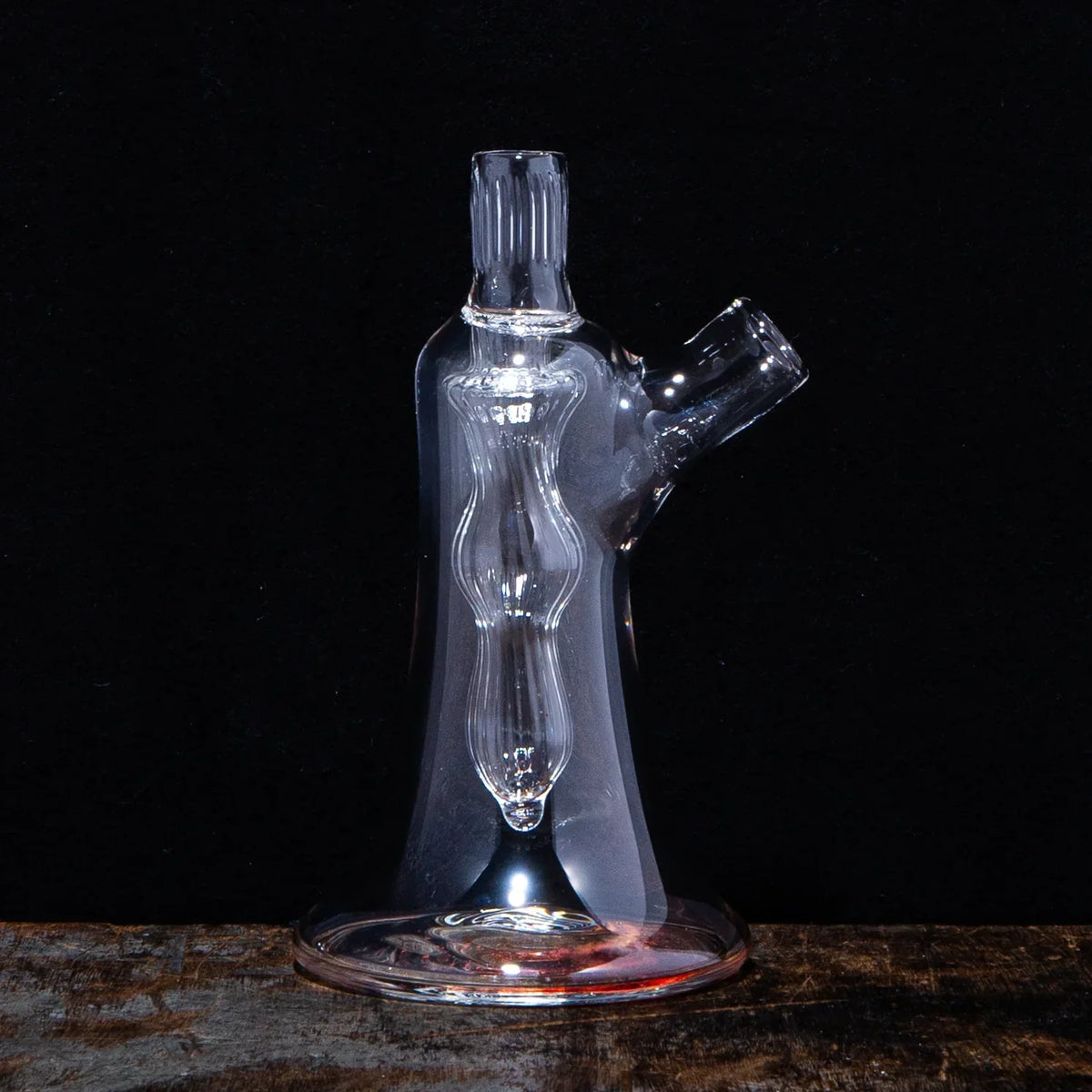 Clear glass water pipe with sculpted body on wooden surface, black background