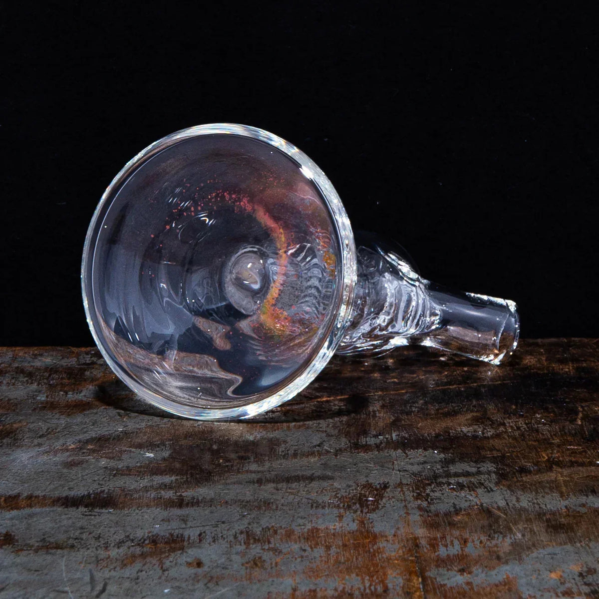 Clear glass smoking bowl with a flared mouthpiece on rustic wood surface