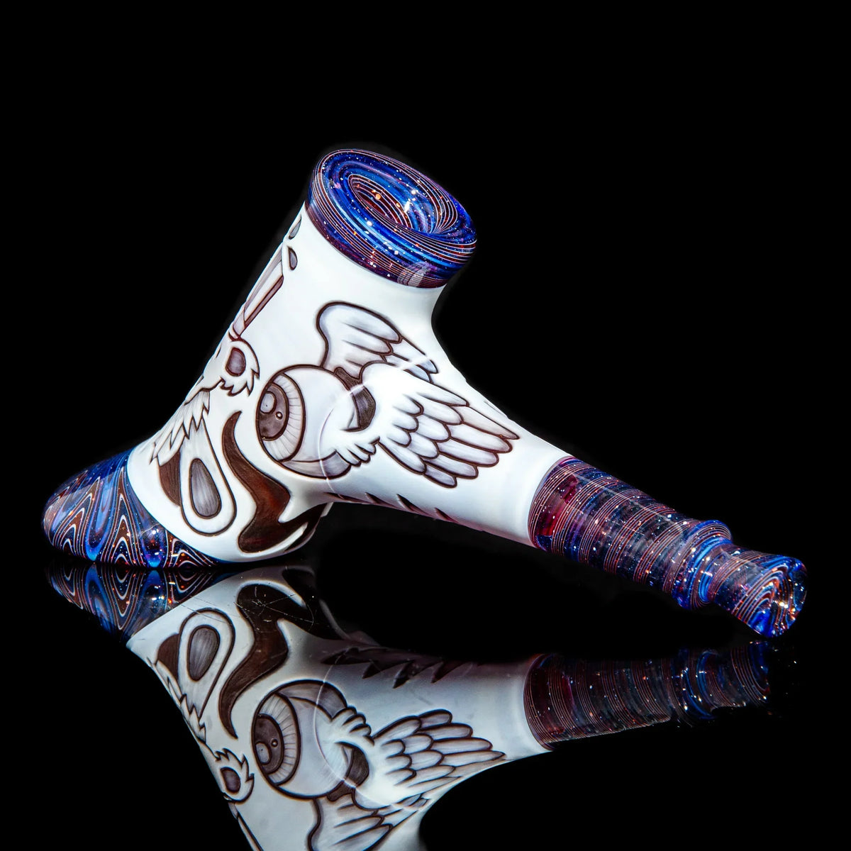 Heady glass hand pipe with intricate eyeball and wing artwork on white, reflective black background