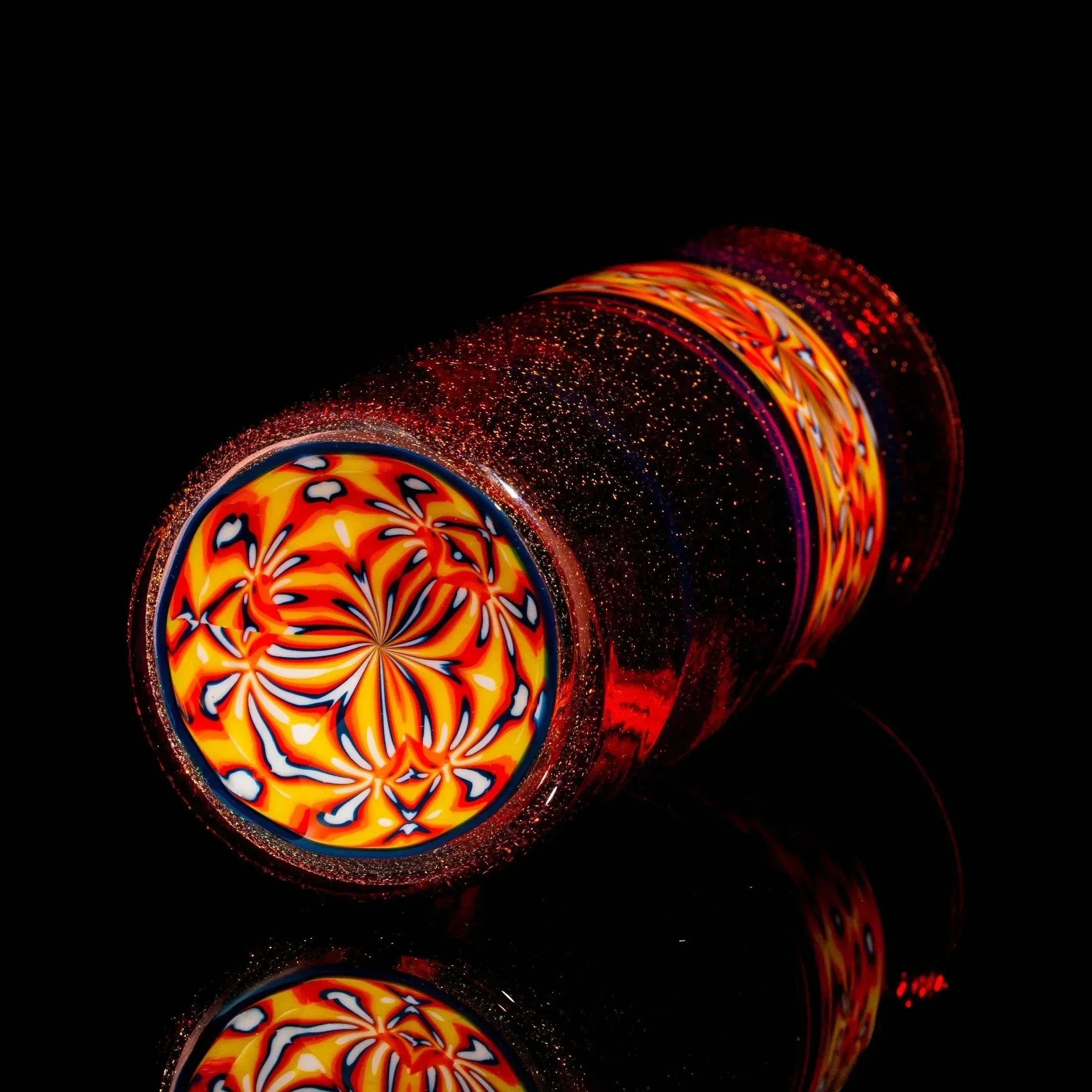 Heady glass tumbler with vibrant orange, blue, and yellow patterned base on black background