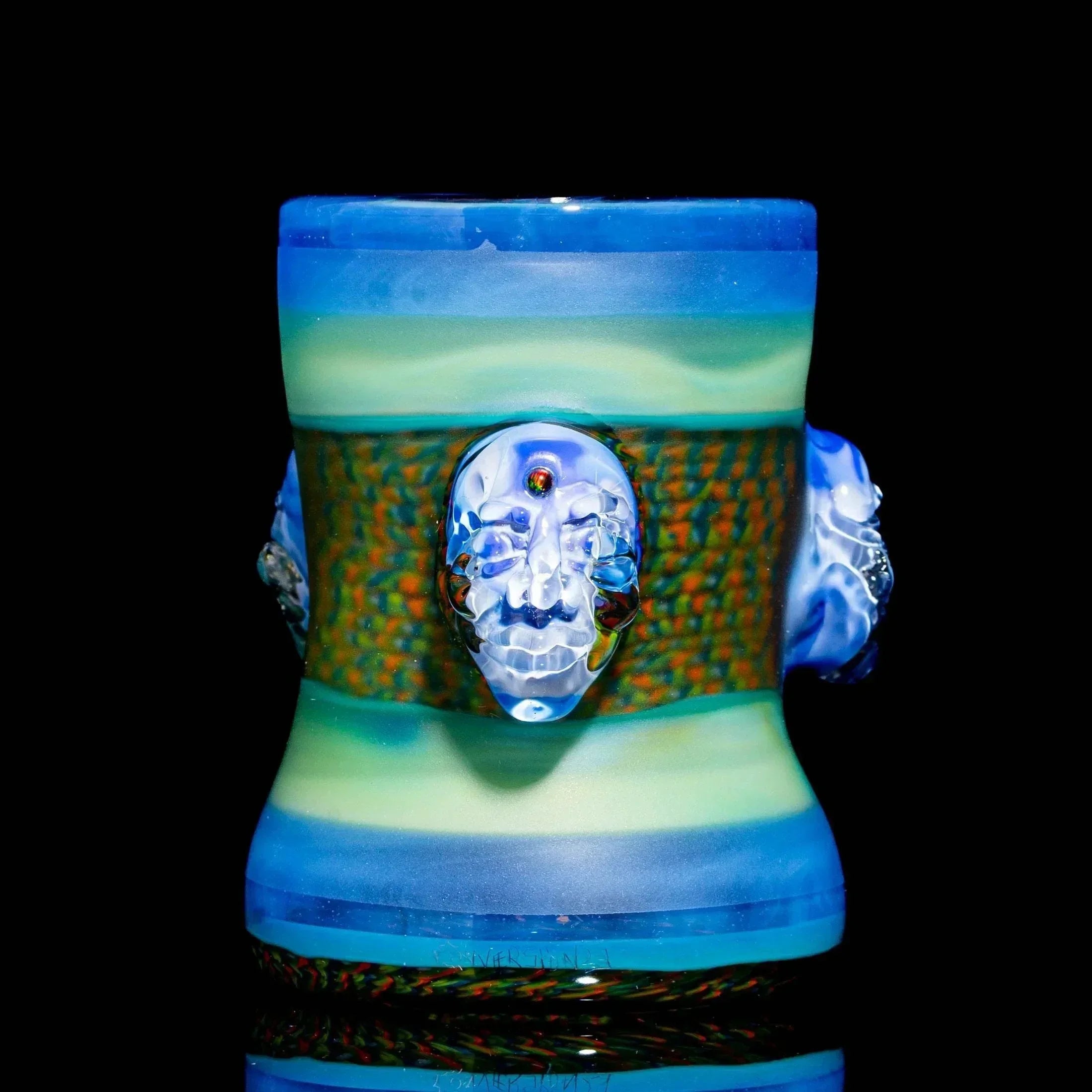 Handcrafted glass drinking vessel with blue-green bands and sculpted face accents