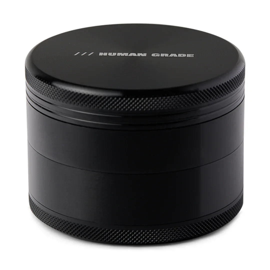 Black metal herb grinder with 'HUMAN GRADE' text engraved on the lid