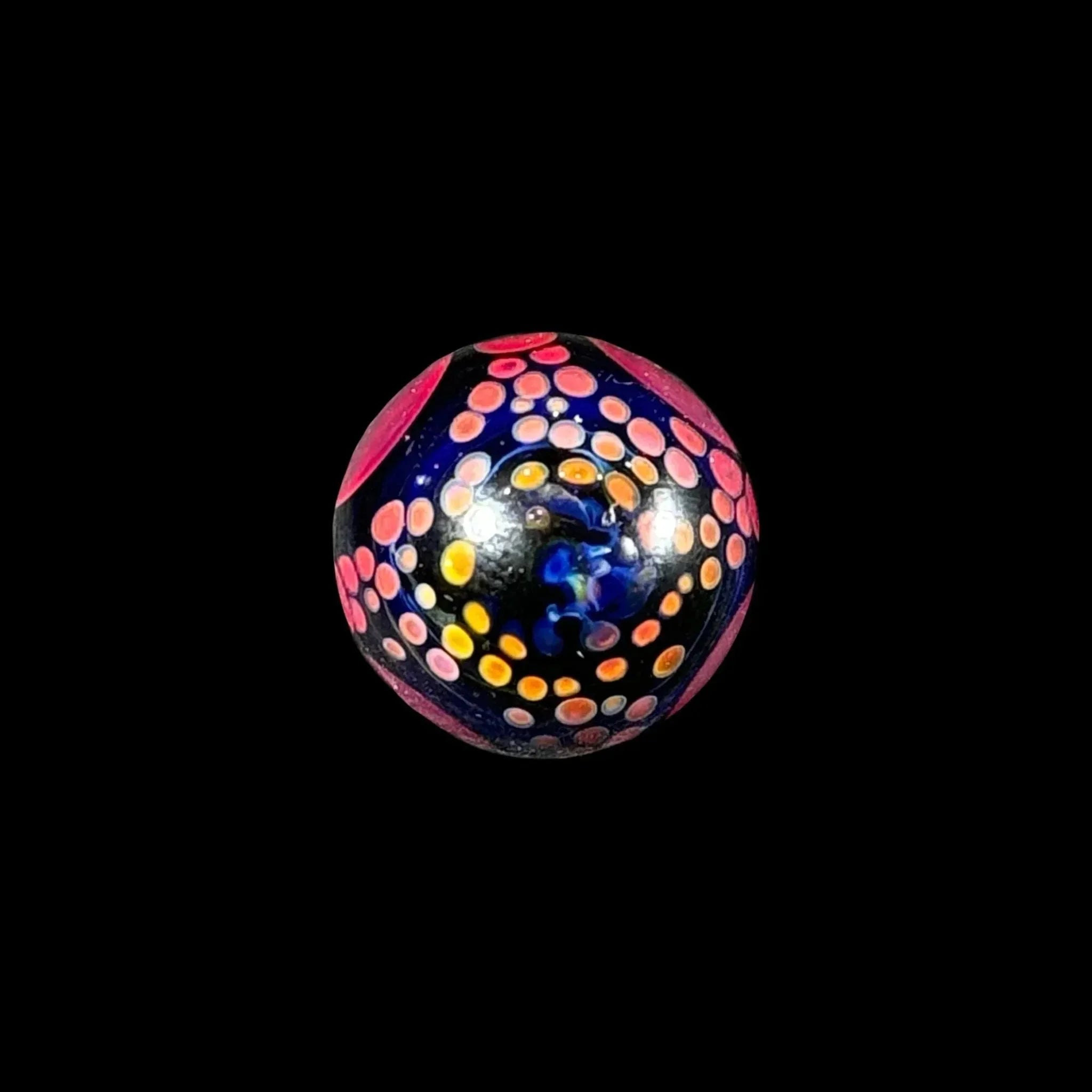 Colorful glass marble with vibrant pink, orange, and blue dot pattern on black background