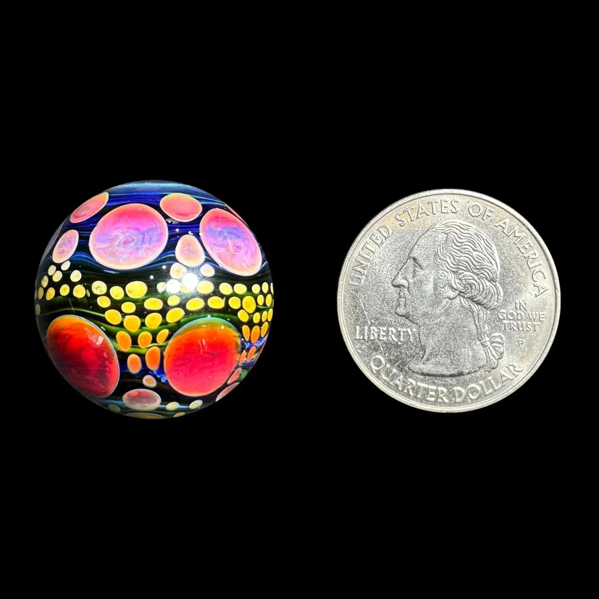 Colorful glass marble with vibrant bubble pattern next to a US quarter for size reference