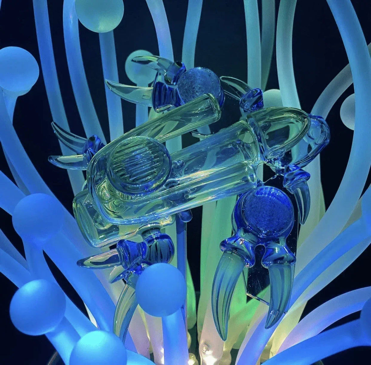 Artistic glass pipe shaped like a crab with glowing blue and green accents, heady glass accessory