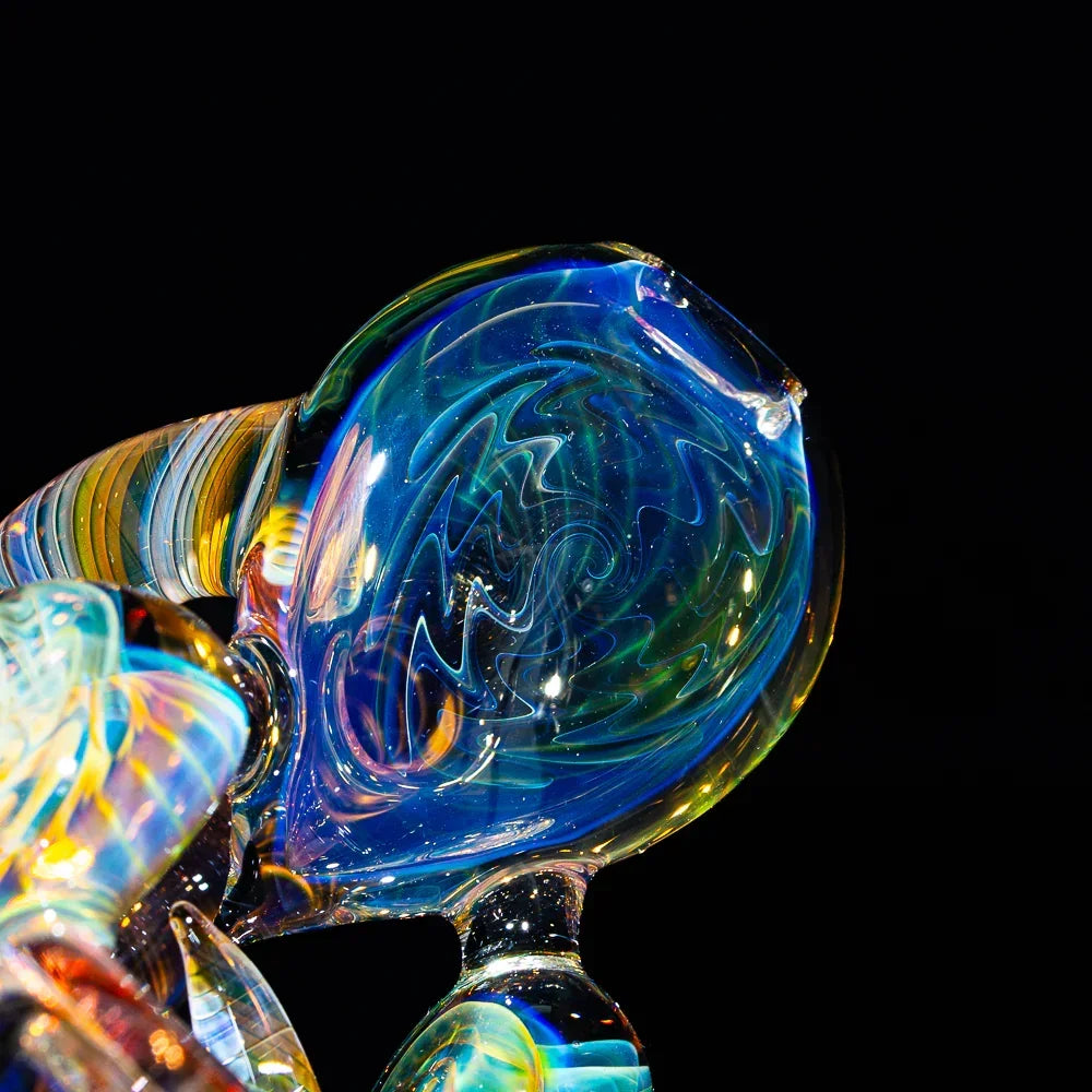 Close-up of heady glass hand pipe with colorful fume and wig wag patterns on black background