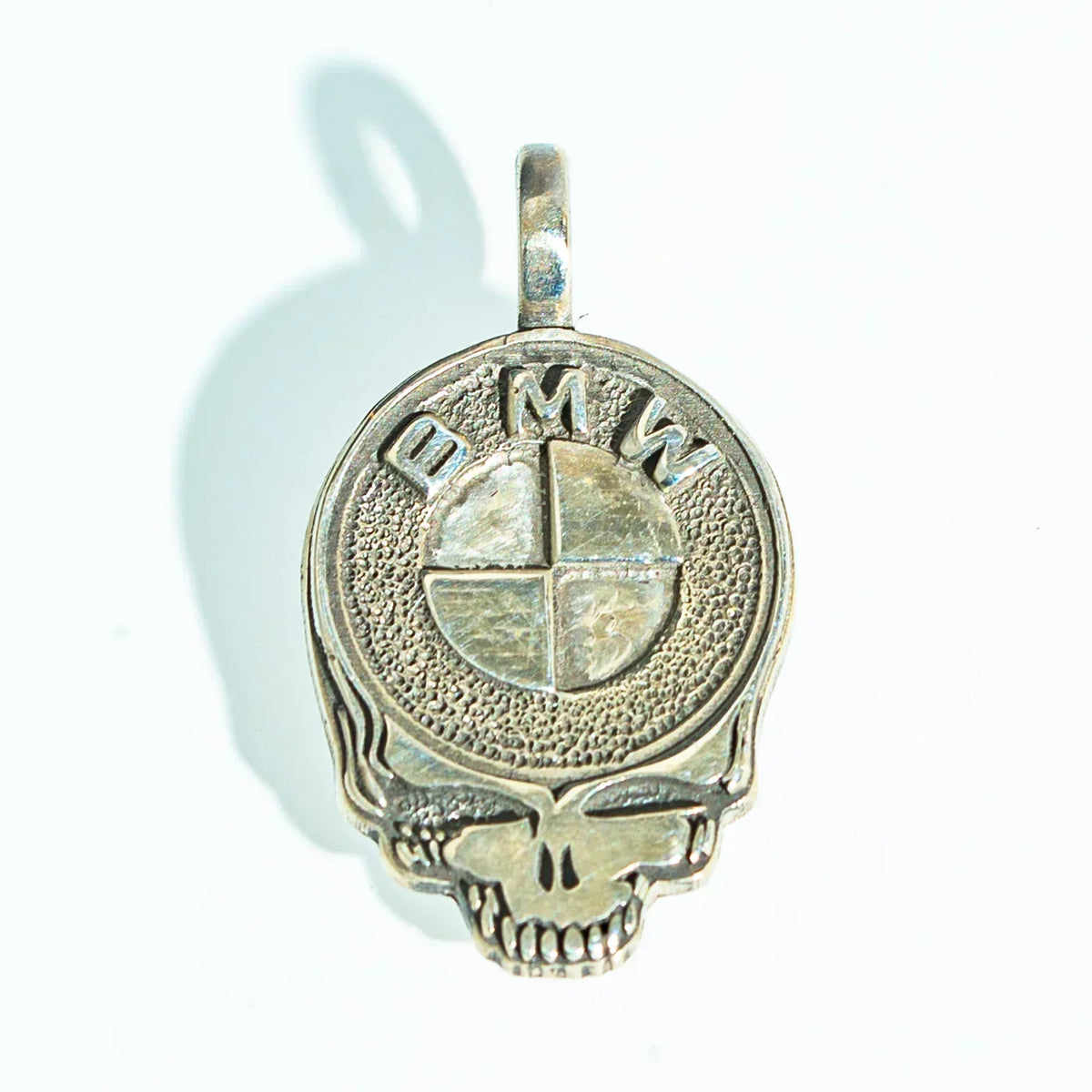 Silver skull pendant with BMW logo design, textured metal, jewelry on white background