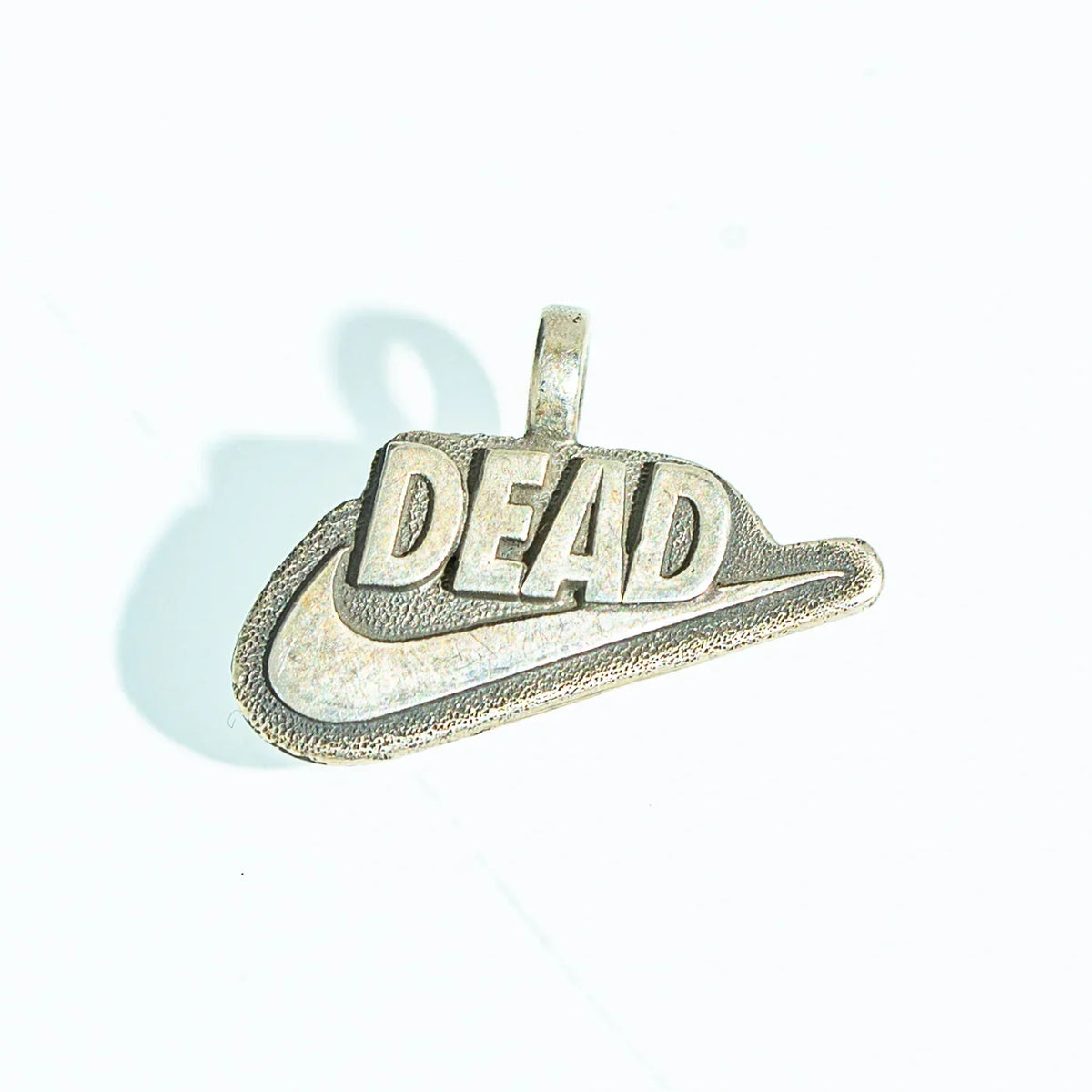 Silver pendant with 'DEAD' text and swoosh design, minimalist jewelry on white background
