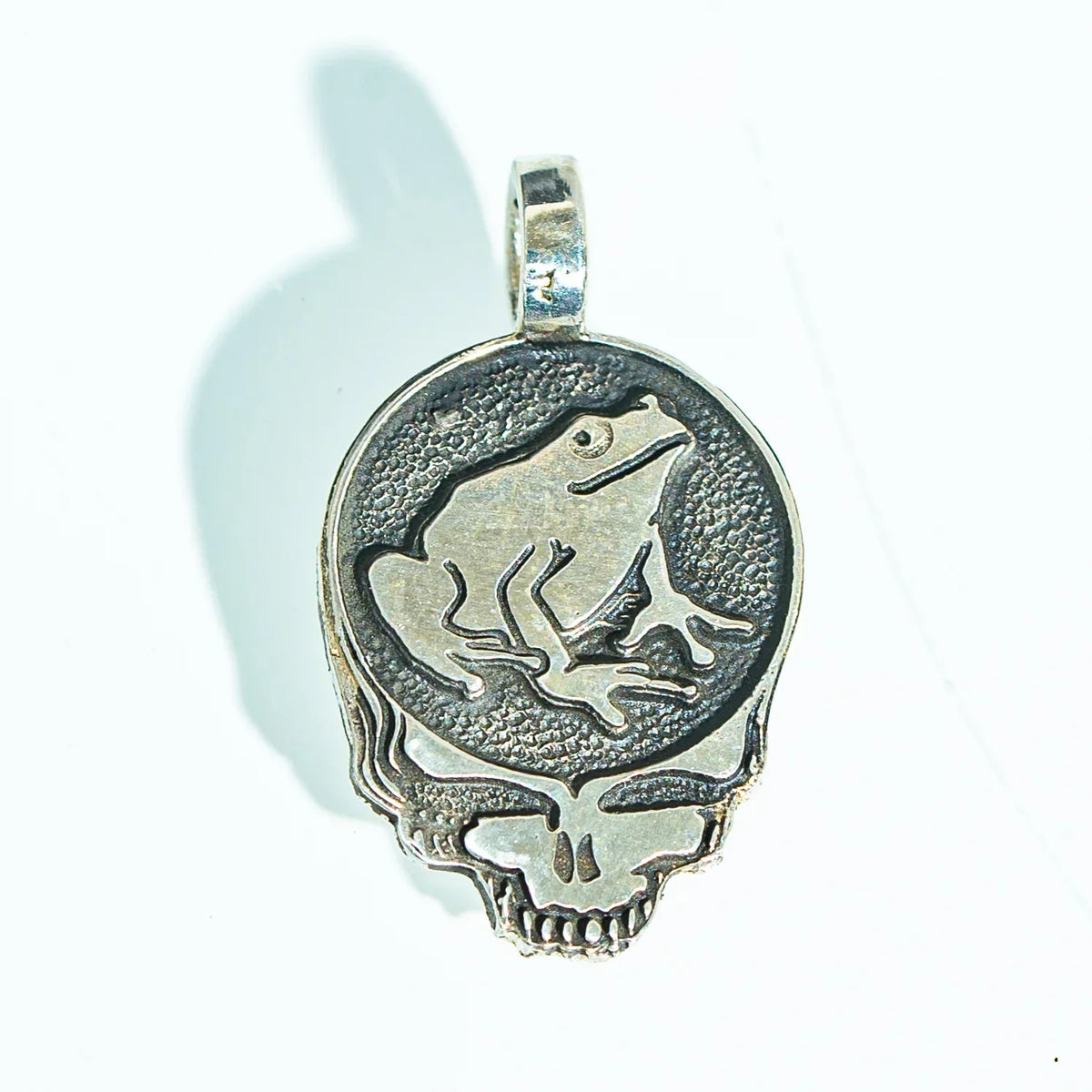 Silver pendant featuring a frog atop a textured skull design on a white background