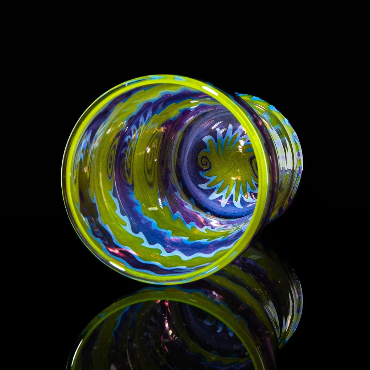Colorful glass cup with purple and green wig wag pattern on black background