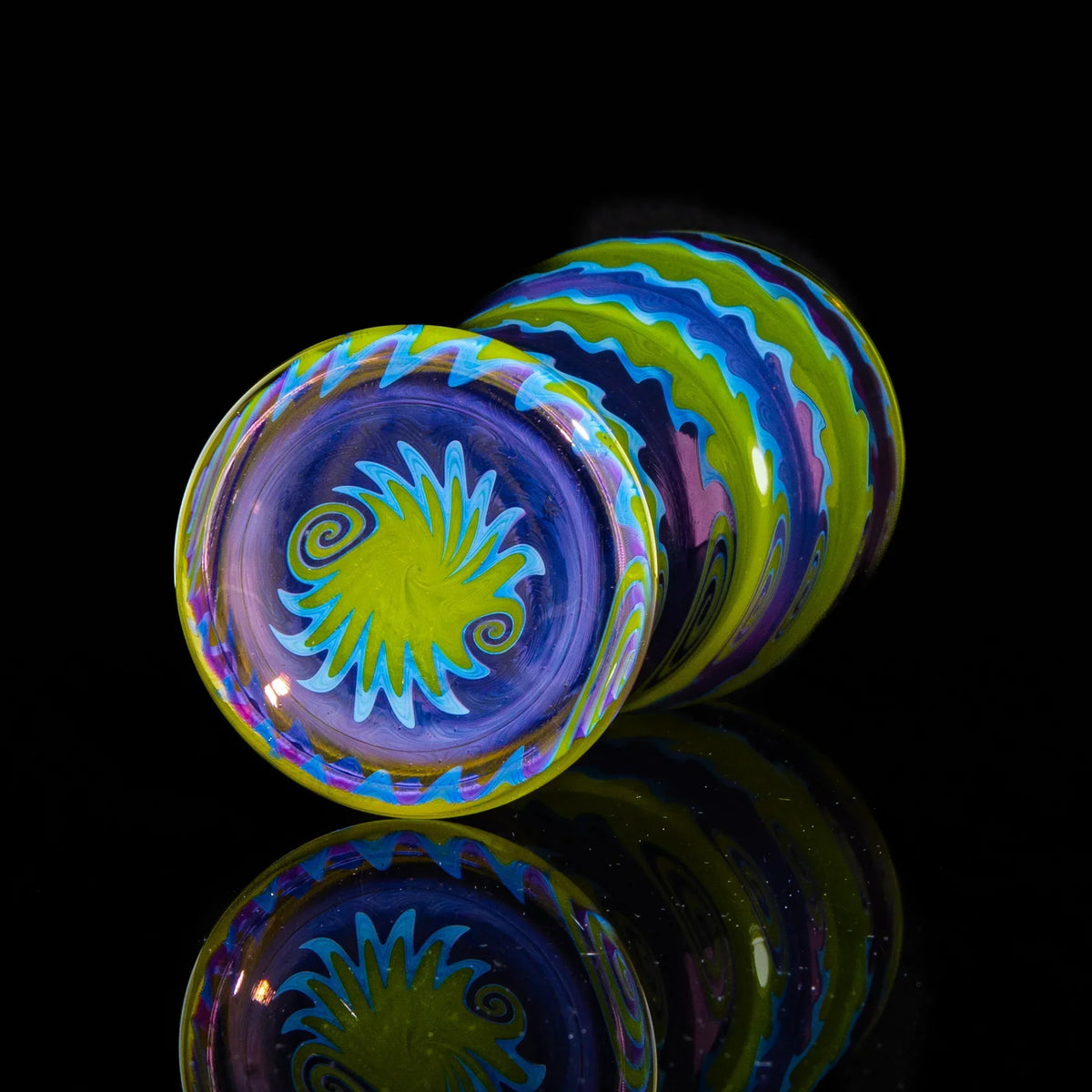 Fully worked glass cup with vibrant purple, green, and blue wig wag patterns on black background