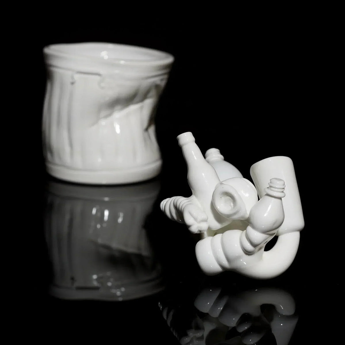 White artistic glass sculpture with bottles and a textured cup on a black reflective surface