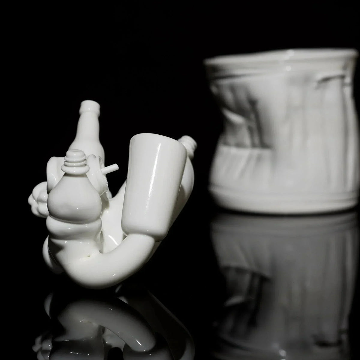 White artistic glass pipe and sculpted container on black reflective surface