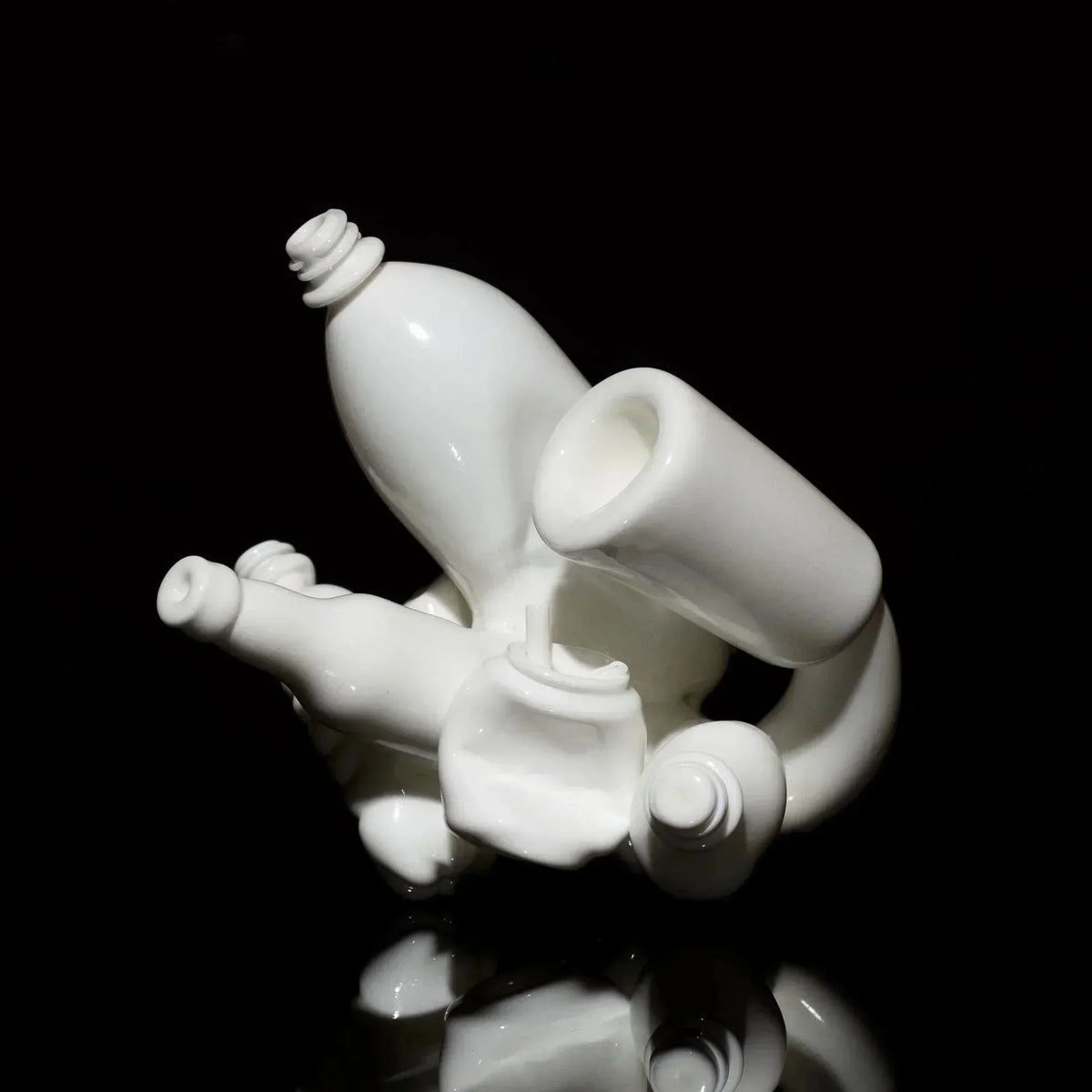 Abstract white glass sculpture with bottle shapes, photographed on a black reflective surface.