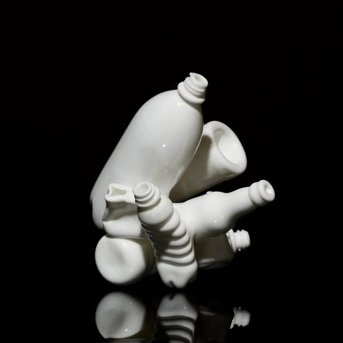 White glass art sculpture with bottle and organic shapes on black background