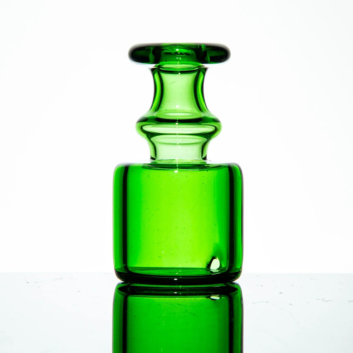 Green glass vaporizer attachment with smooth, curved design on reflective surface