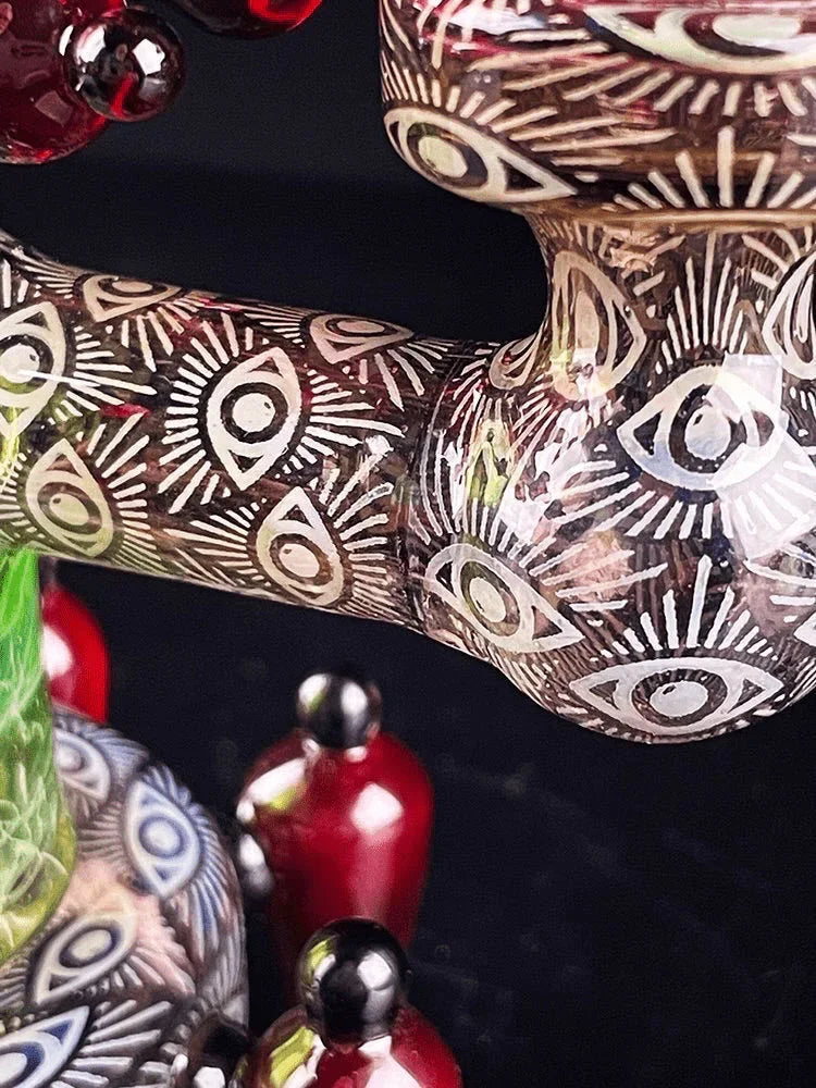 Intricate glass water pipe with all-seeing eye patterns and colorful red and green accents.