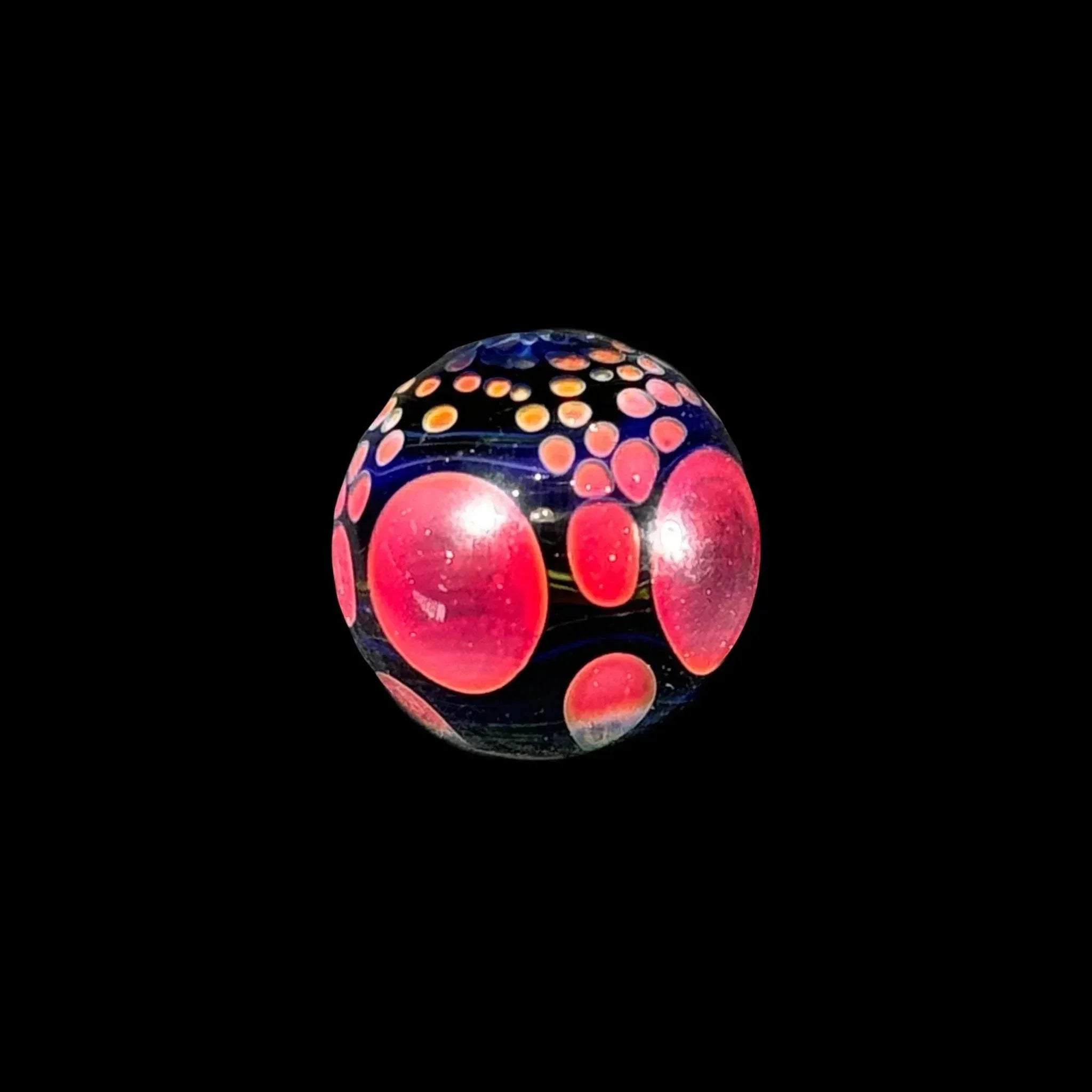 Handcrafted glass marble with red and orange dot patterns on a black background