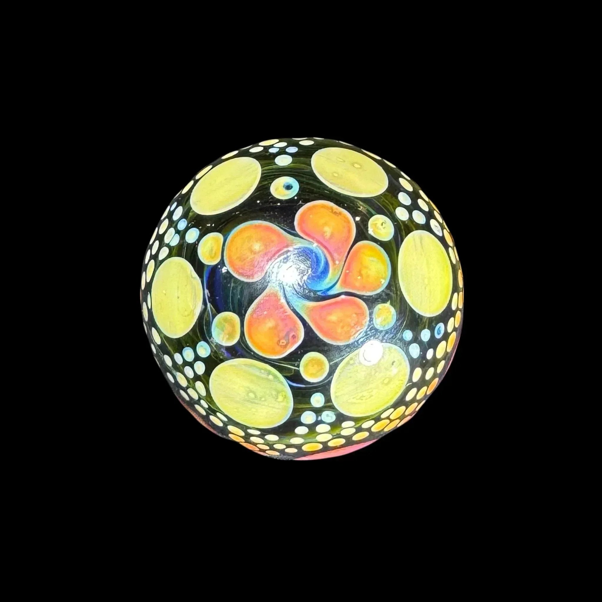 Hand-blown glass marble with vibrant yellow, orange, and blue psychedelic patterns on black background
