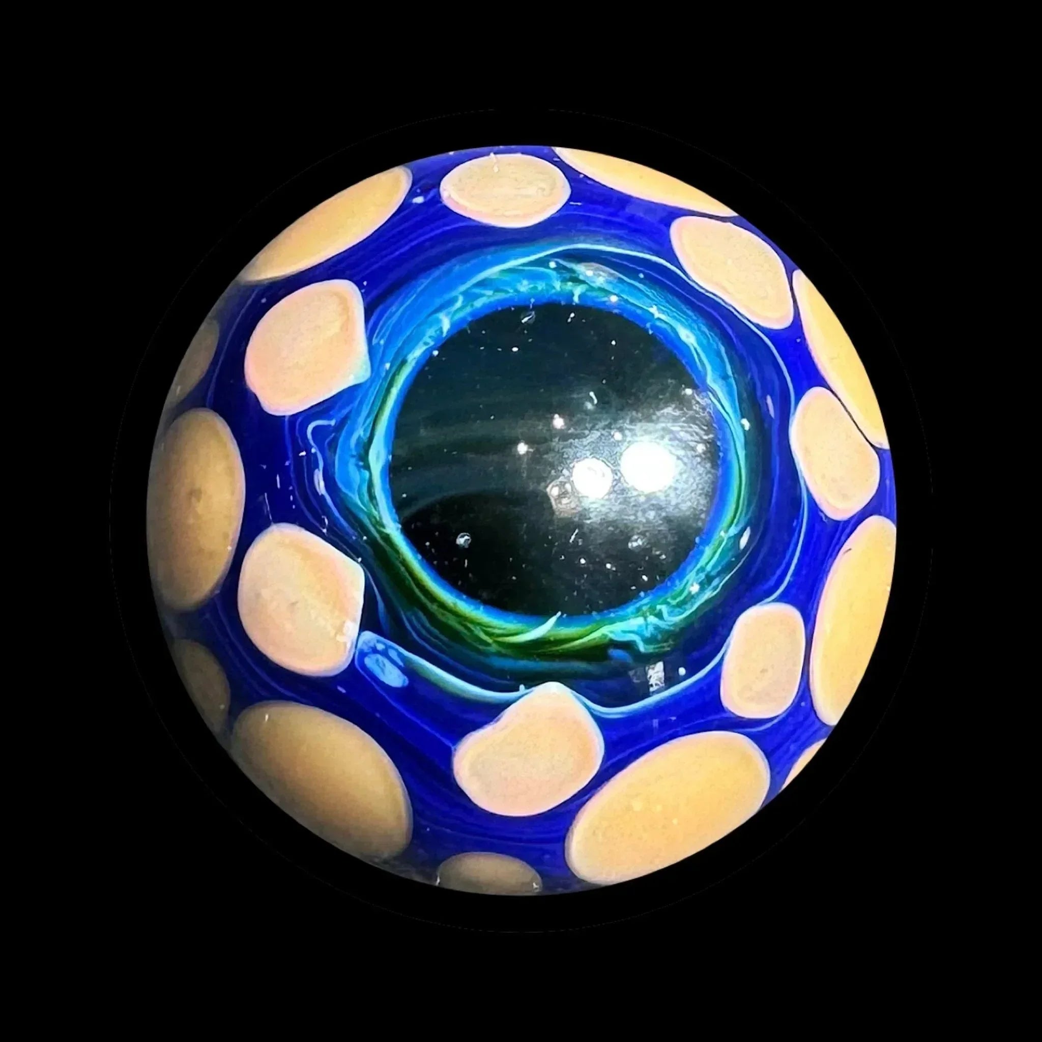 Hand-blown glass marble with blue, yellow, and black eye-inspired design on black background
