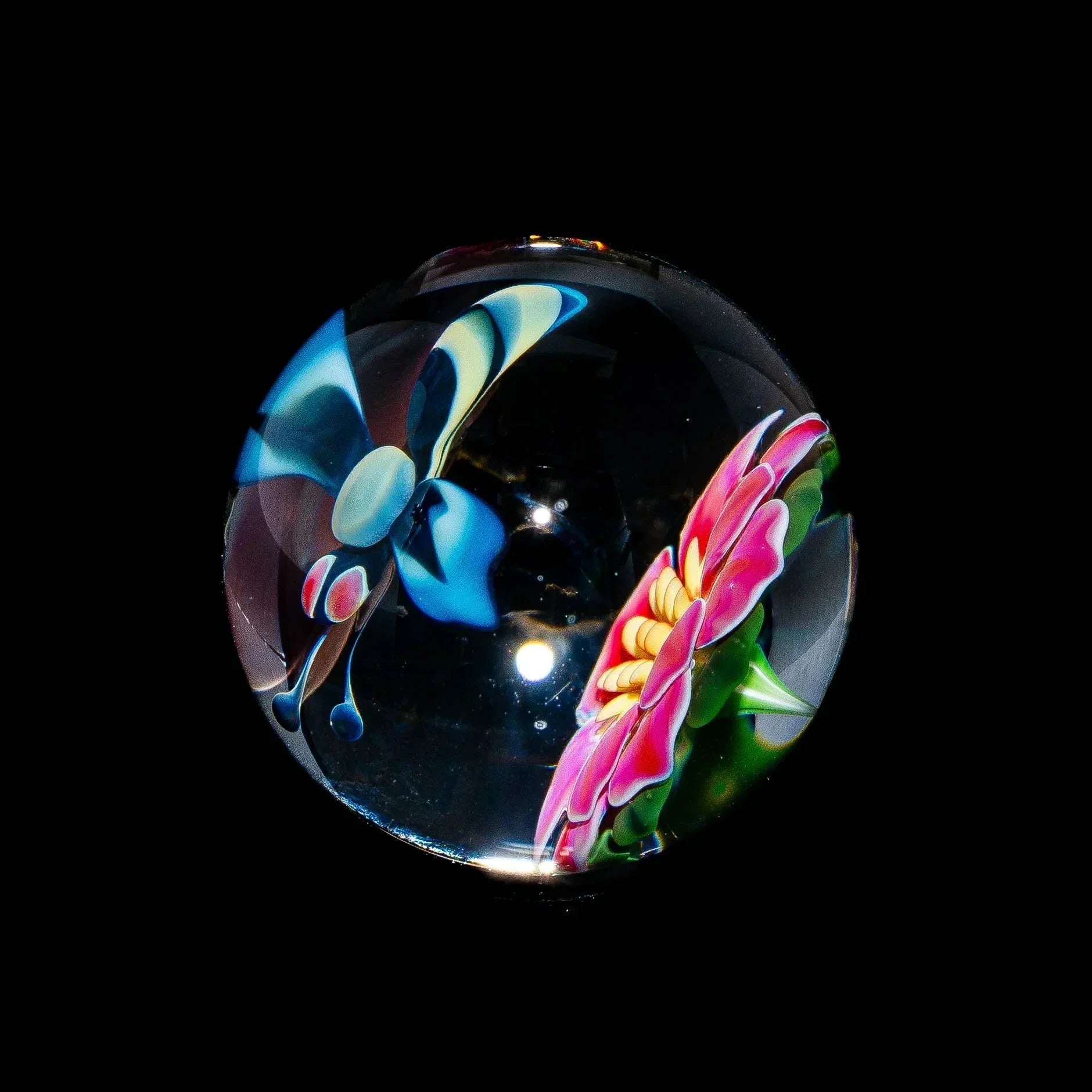 Glass marble with detailed blue bee and pink flower art on black background