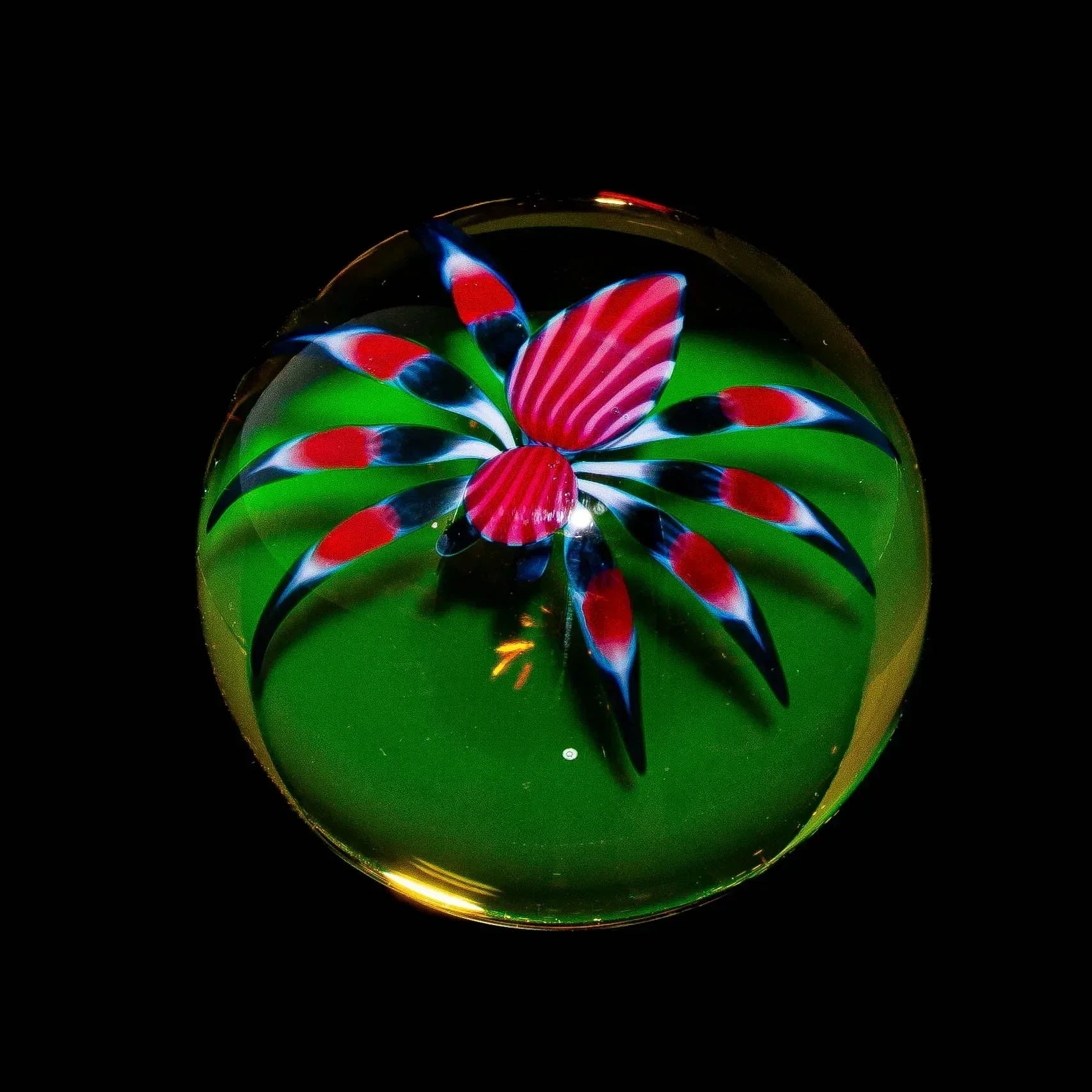 Handcrafted glass marble featuring a red and black striped spider design on green background