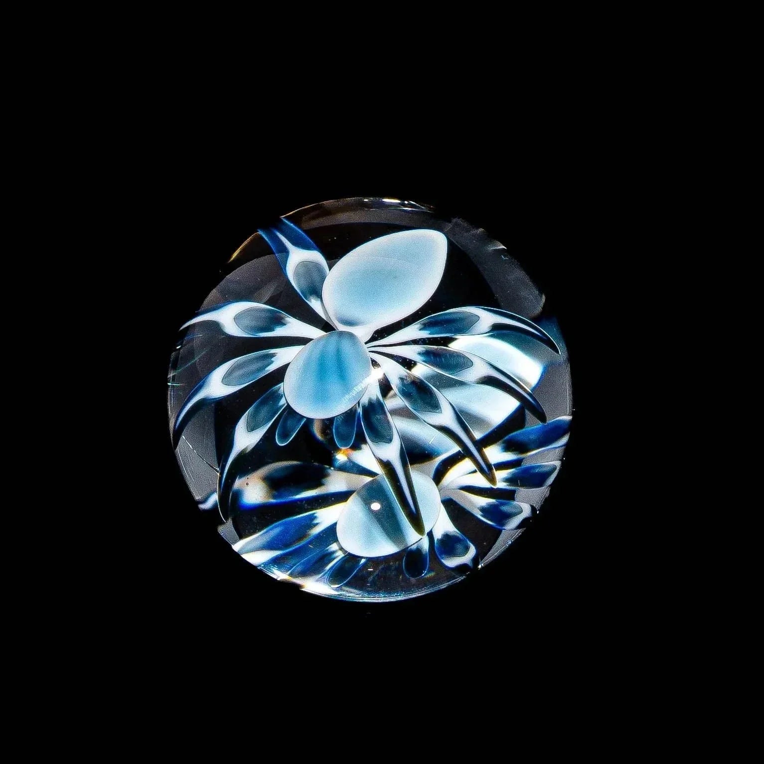 Handcrafted glass marble with intricate blue and white flower-like design on black background
