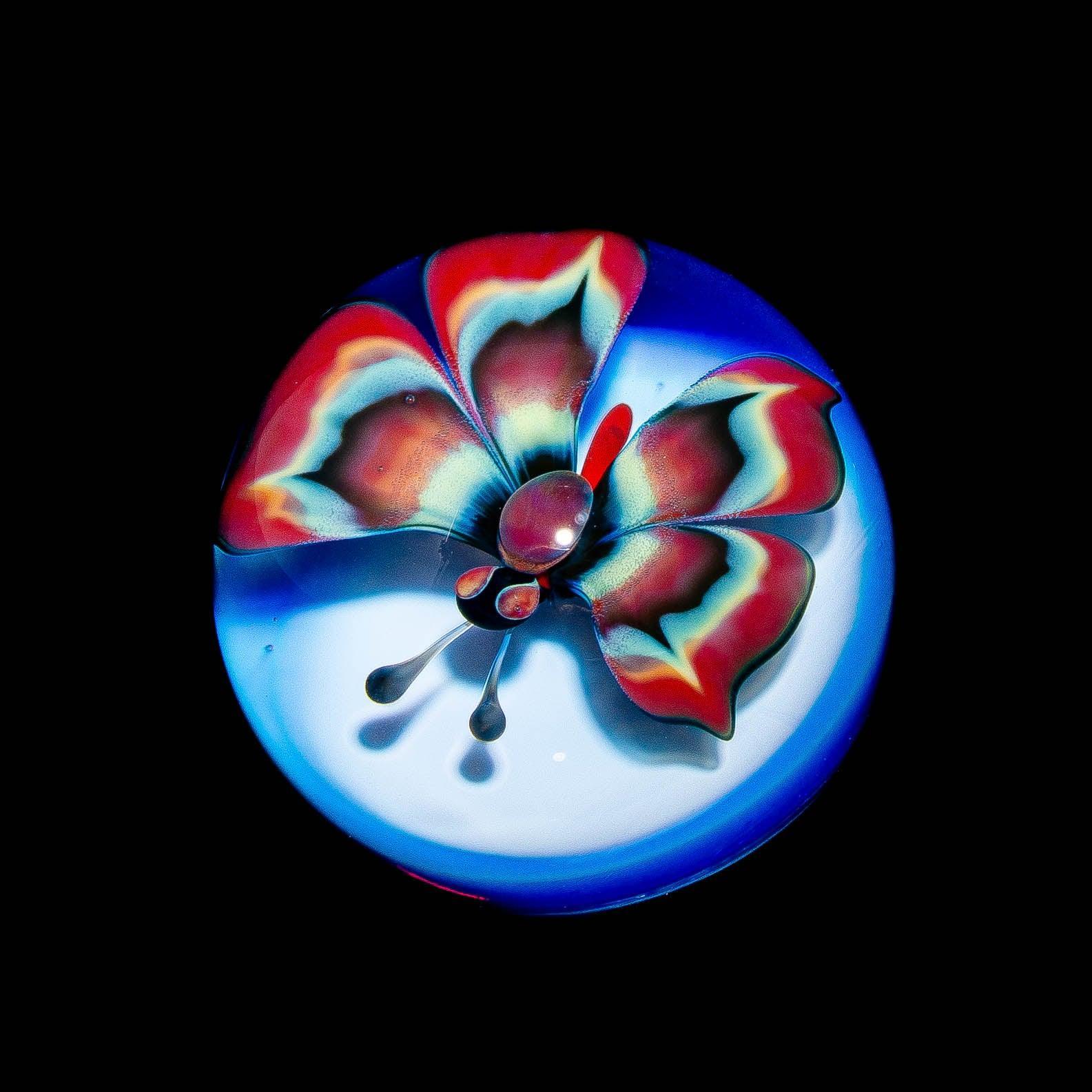 Colorful tie-dye glass butterfly art piece with blue and red wings on a round base