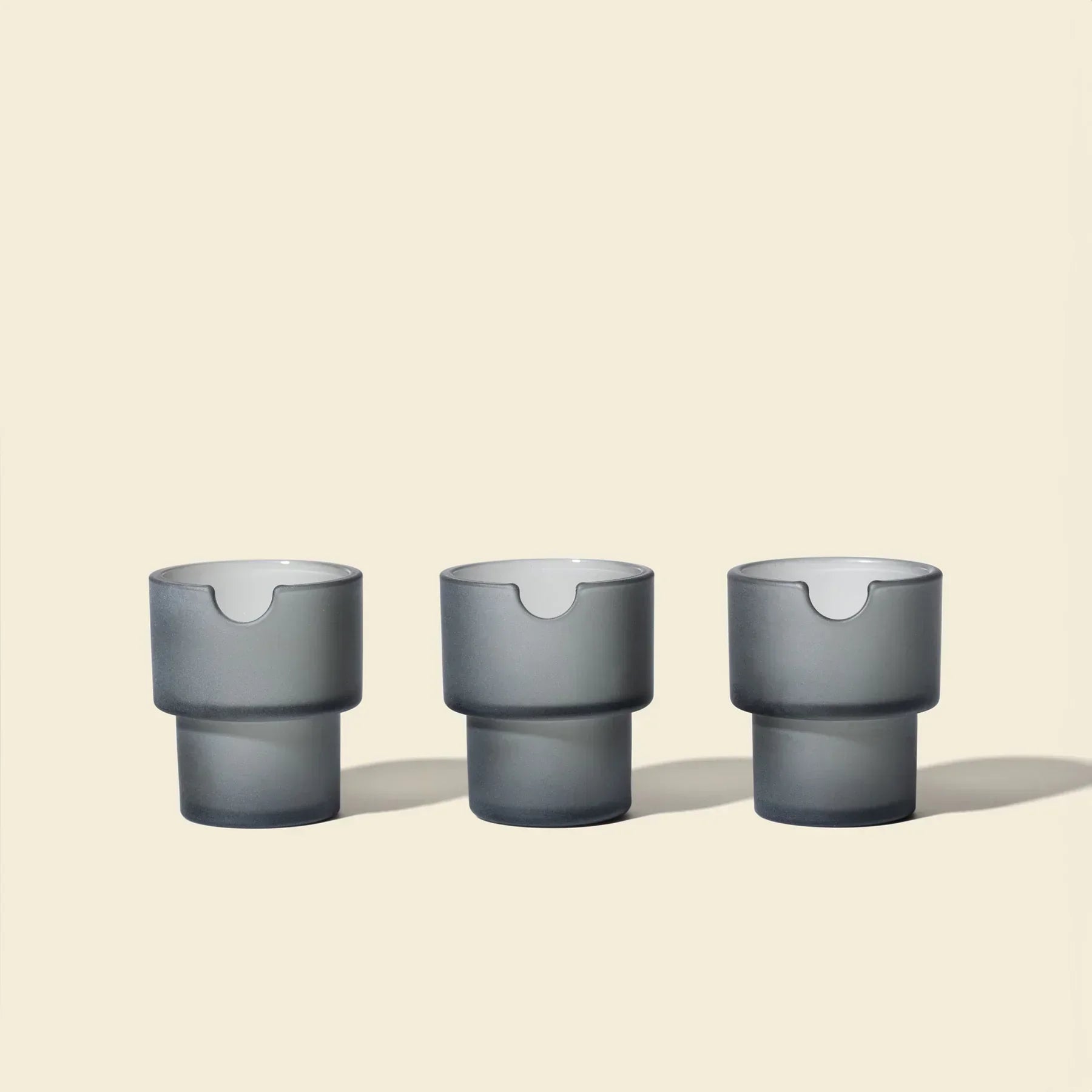 Three modern charcoal gray glass flowerpots with minimalist design on a neutral background