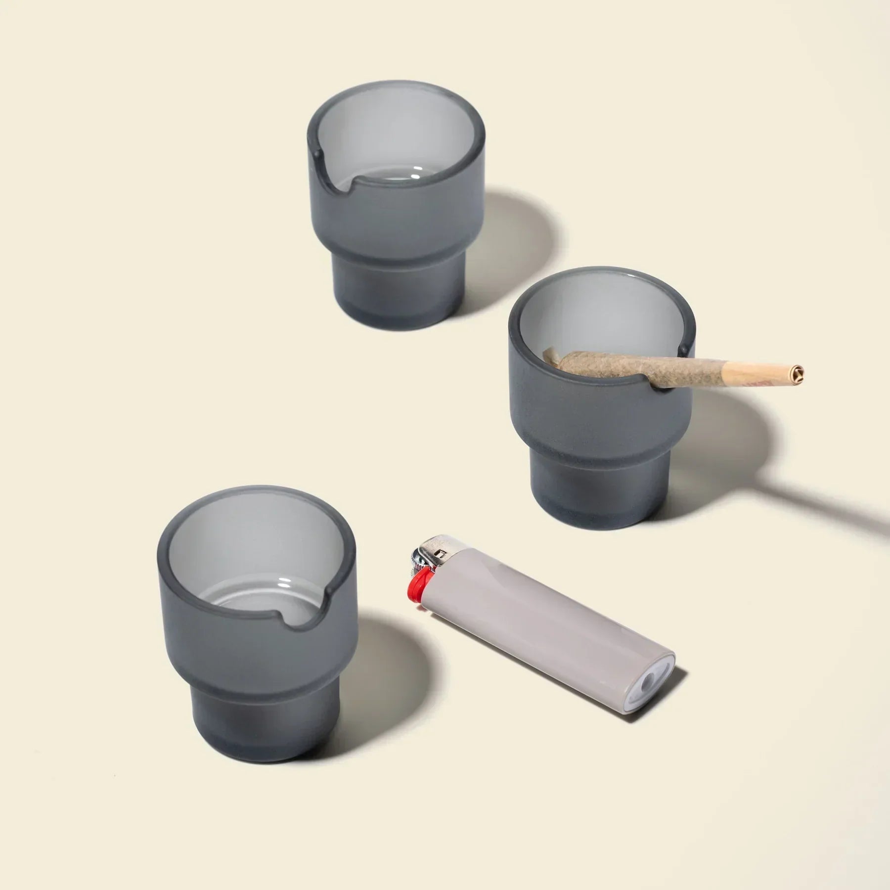 Set of three charcoal glass ashtrays with a lighter and a rolled smoking paper