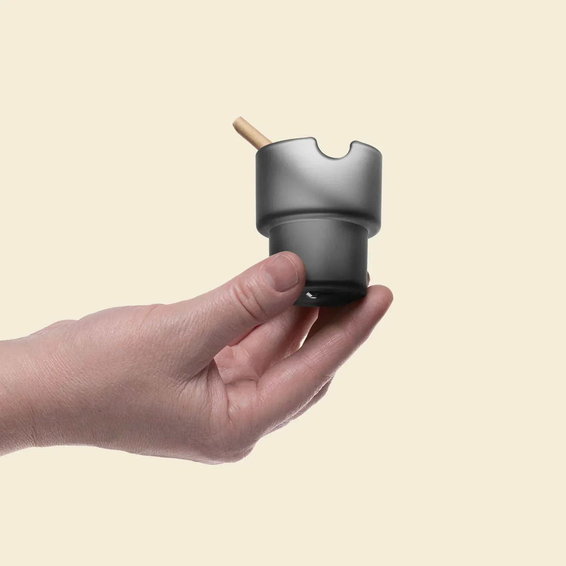 Hand holding a charcoal-colored glass ashtray with a cigarette