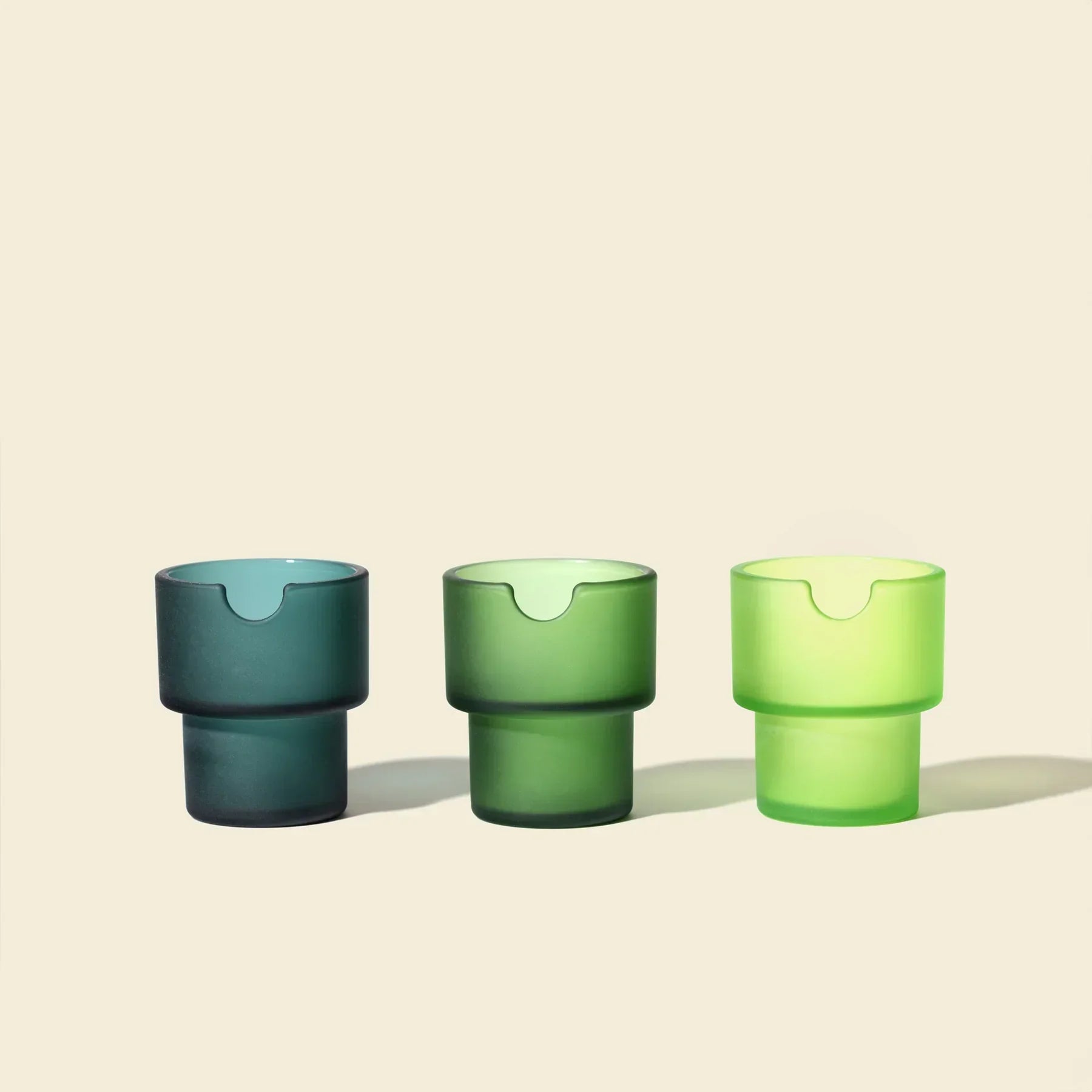 Three modern green glass ashtrays in varying shades on a light background