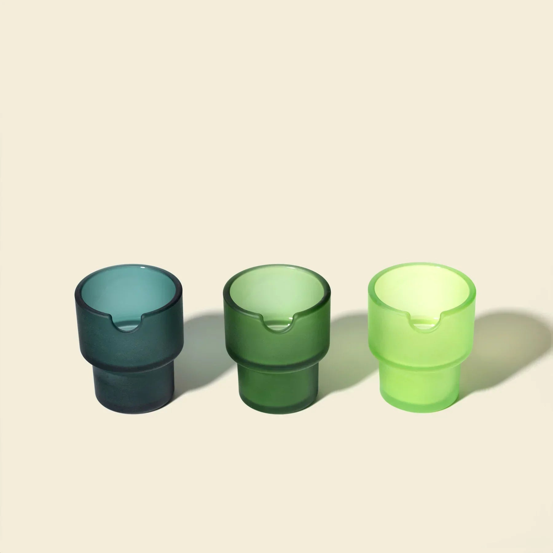 Three modern glass flowerpots in blue, green, and light green on a neutral background