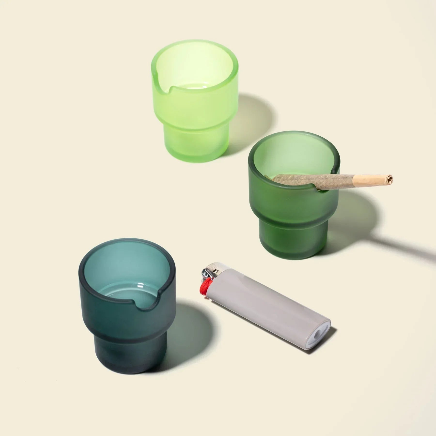 Set of colored glass ashtrays with a pre-rolled cone and a lighter on a light surface