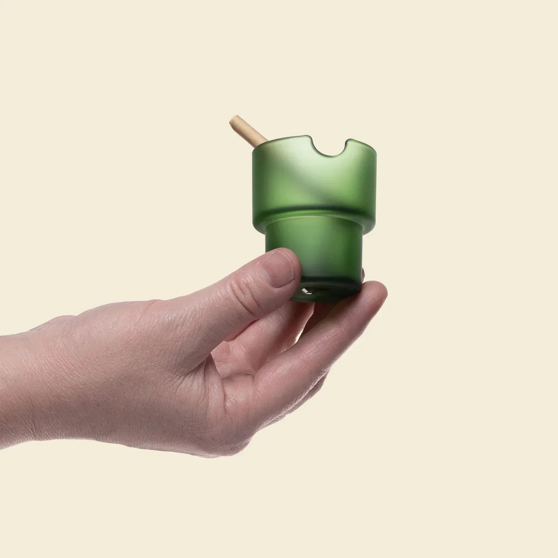 Hand holding a green frosted glass ashtray with a wooden smoking accessory.