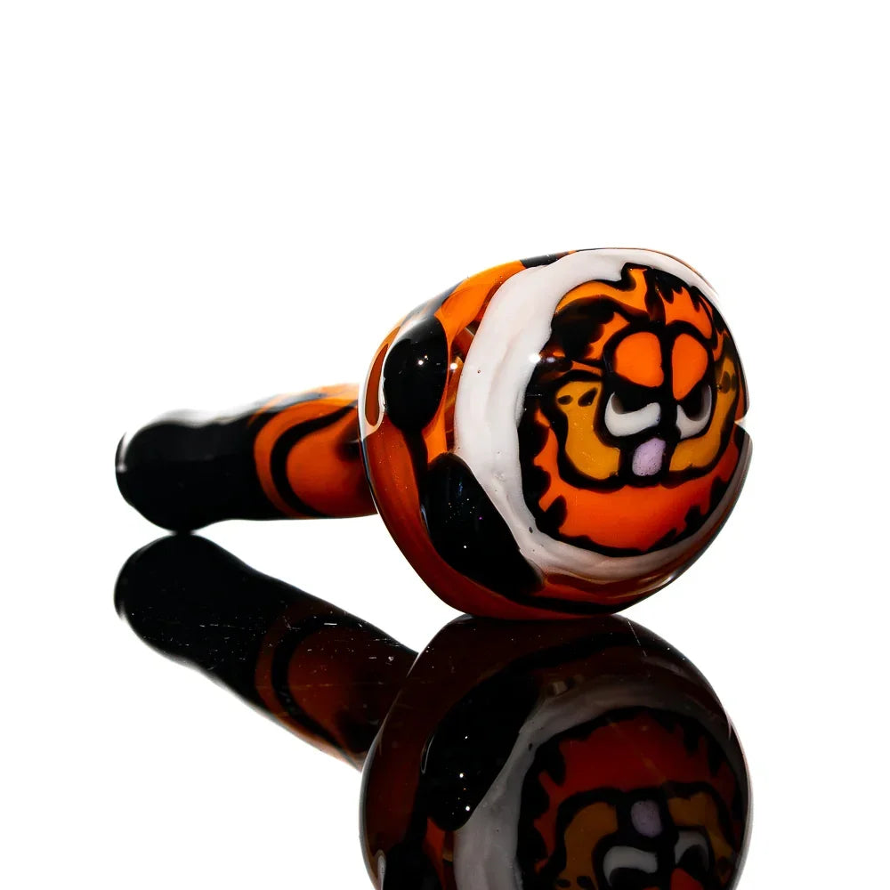 Hand-blown orange glass spoon pipe with cartoon cat face design, displayed on black surface