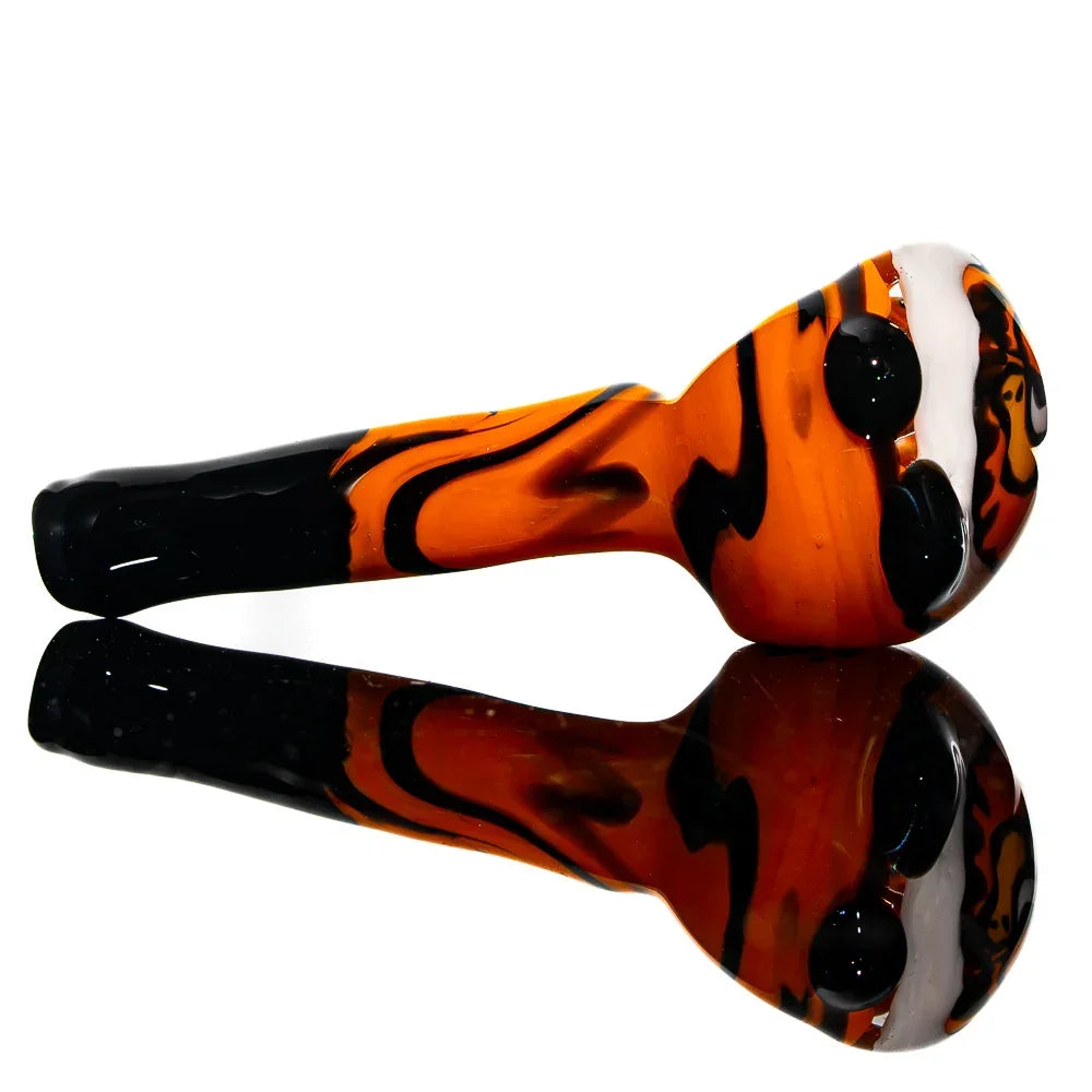Orange and black glass hand pipe with cartoon face design, reflected on black surface