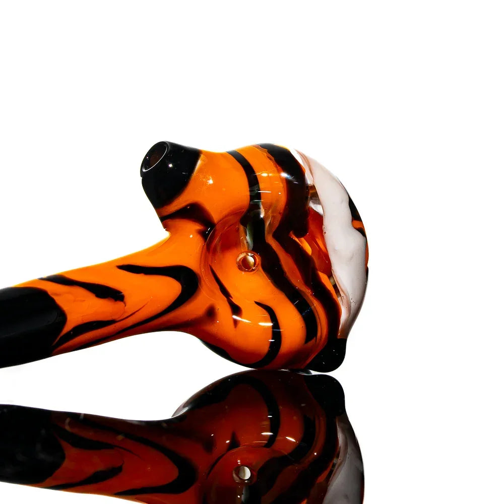 Hand-blown orange and black glass spoon pipe with white accent, reflected on glossy surface