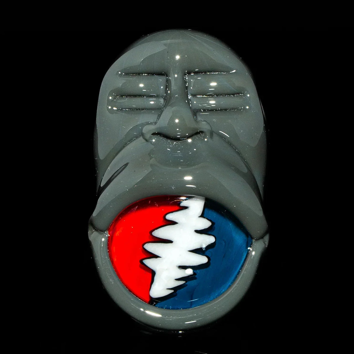 Gray glass pendant shaped like a face with a red, white, and blue zigzag mouth design