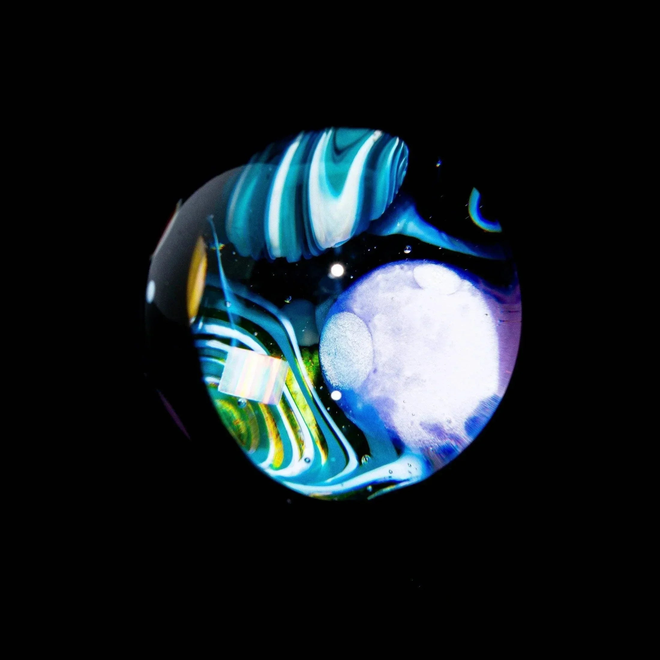 Heady glass marble with swirling blue, green, and white patterns on black background