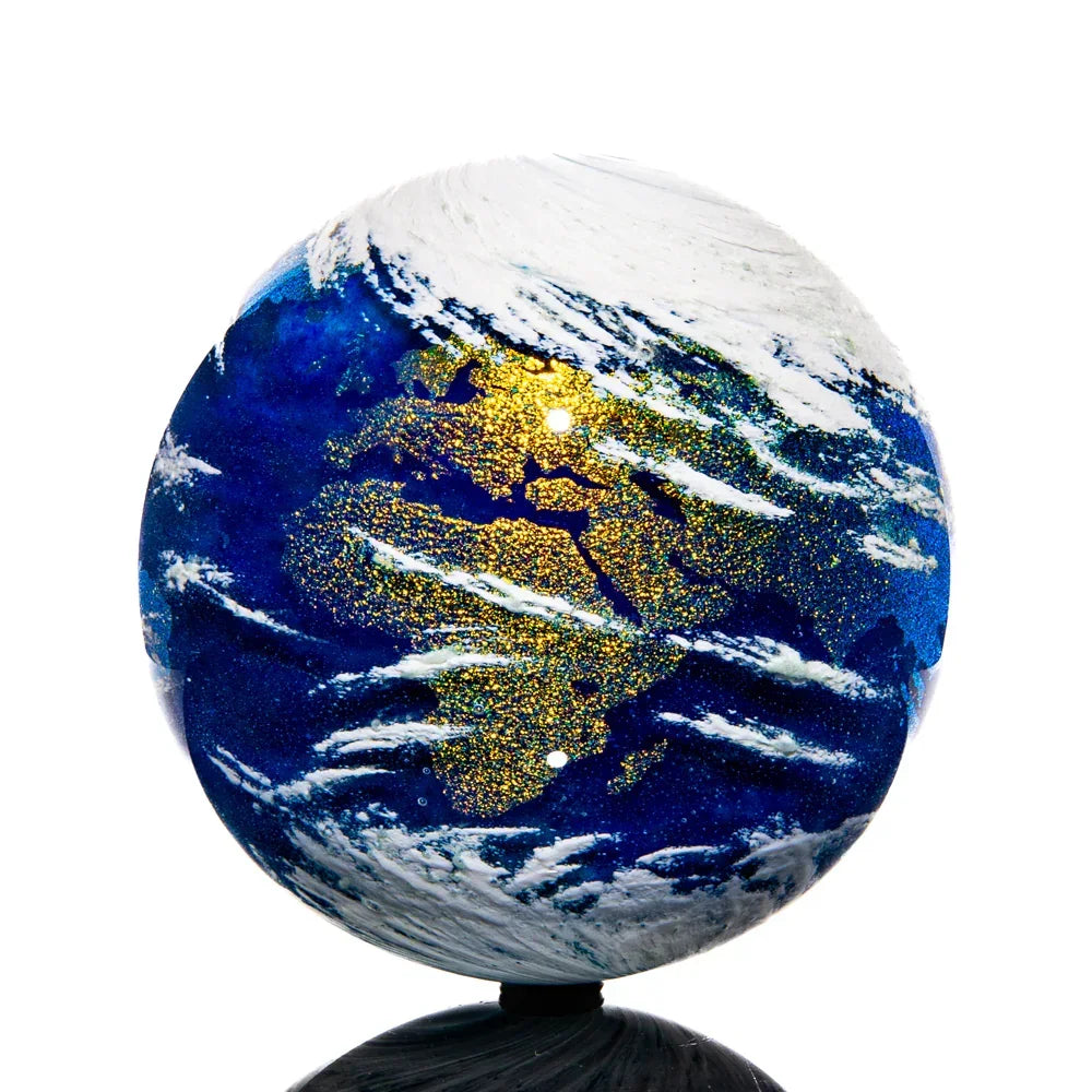 Handblown glass marble featuring a detailed Earth design with swirling blue, gold, and white accents.