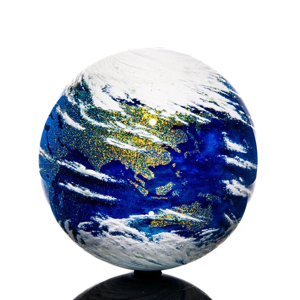 Handcrafted glass art marble with Earth design, blue and gold details, swirling white clouds