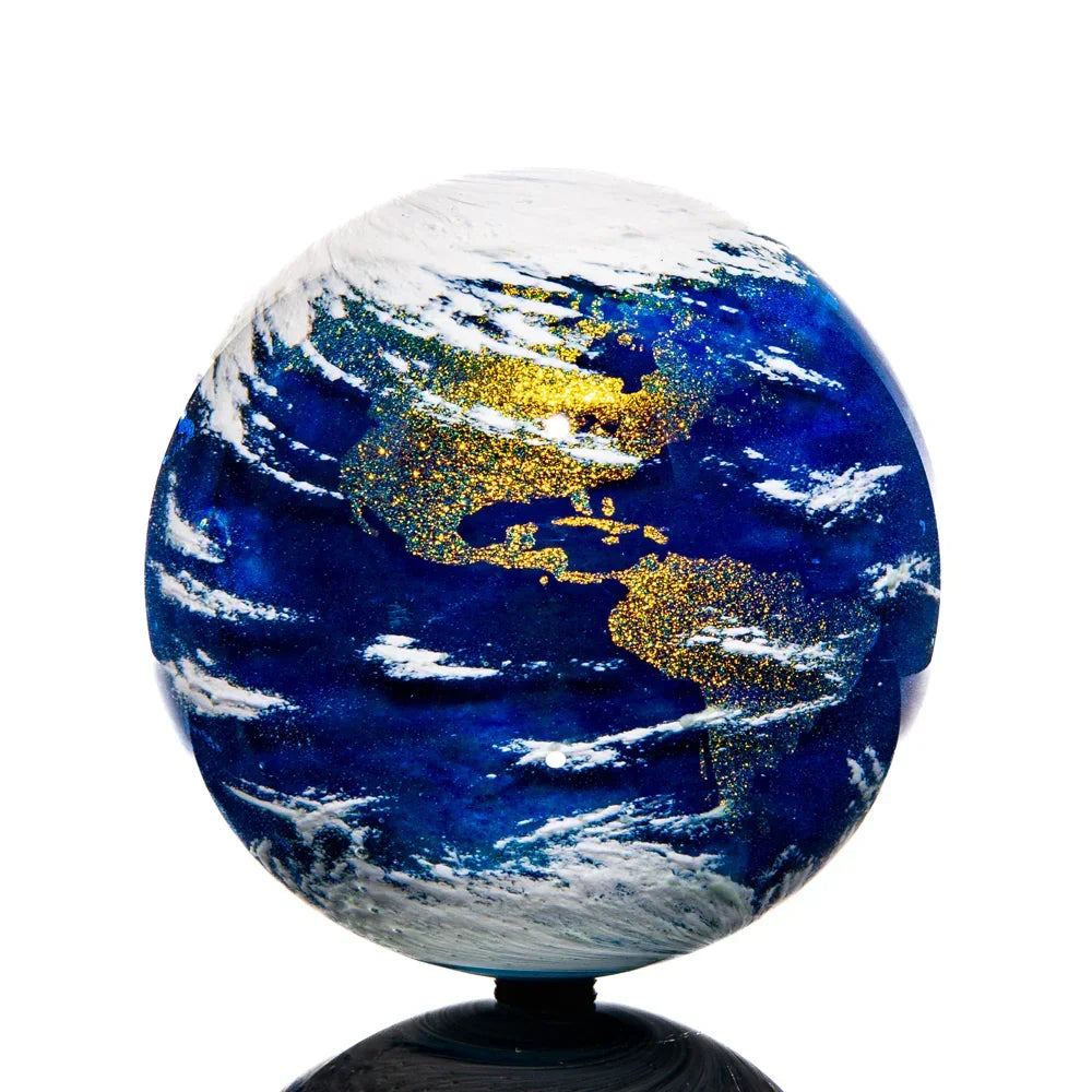 Hand-blown glass Earth marble with blue, gold, and white swirling details on a black base.