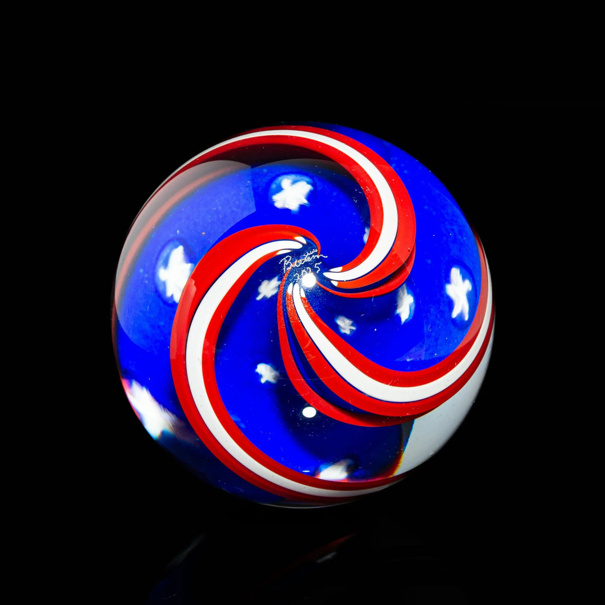 Red, white, and blue art glass marble with swirl and star design on black background