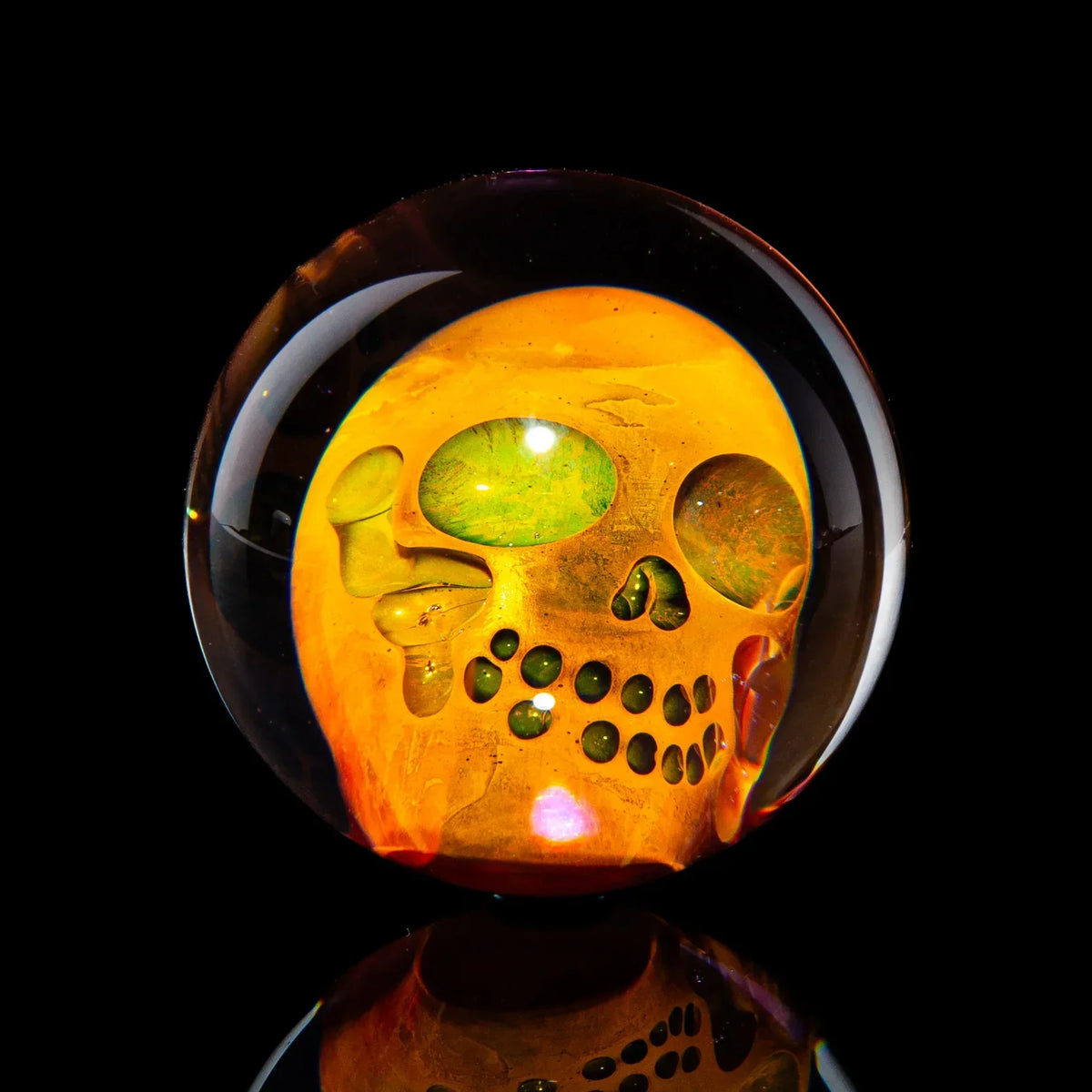 Hand-blown glass marble with detailed orange skull design, reflective black background
