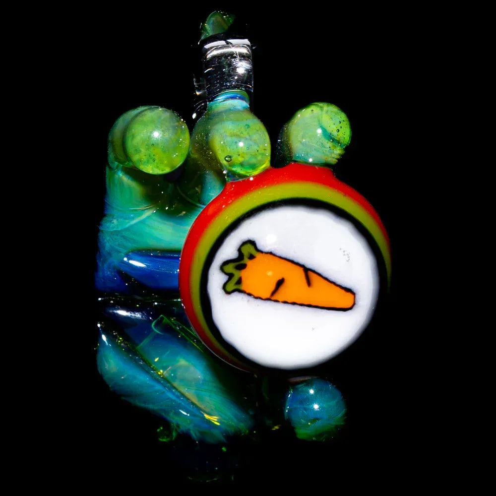 Colorful glass pendant with carrot design held by green glass hand on black background