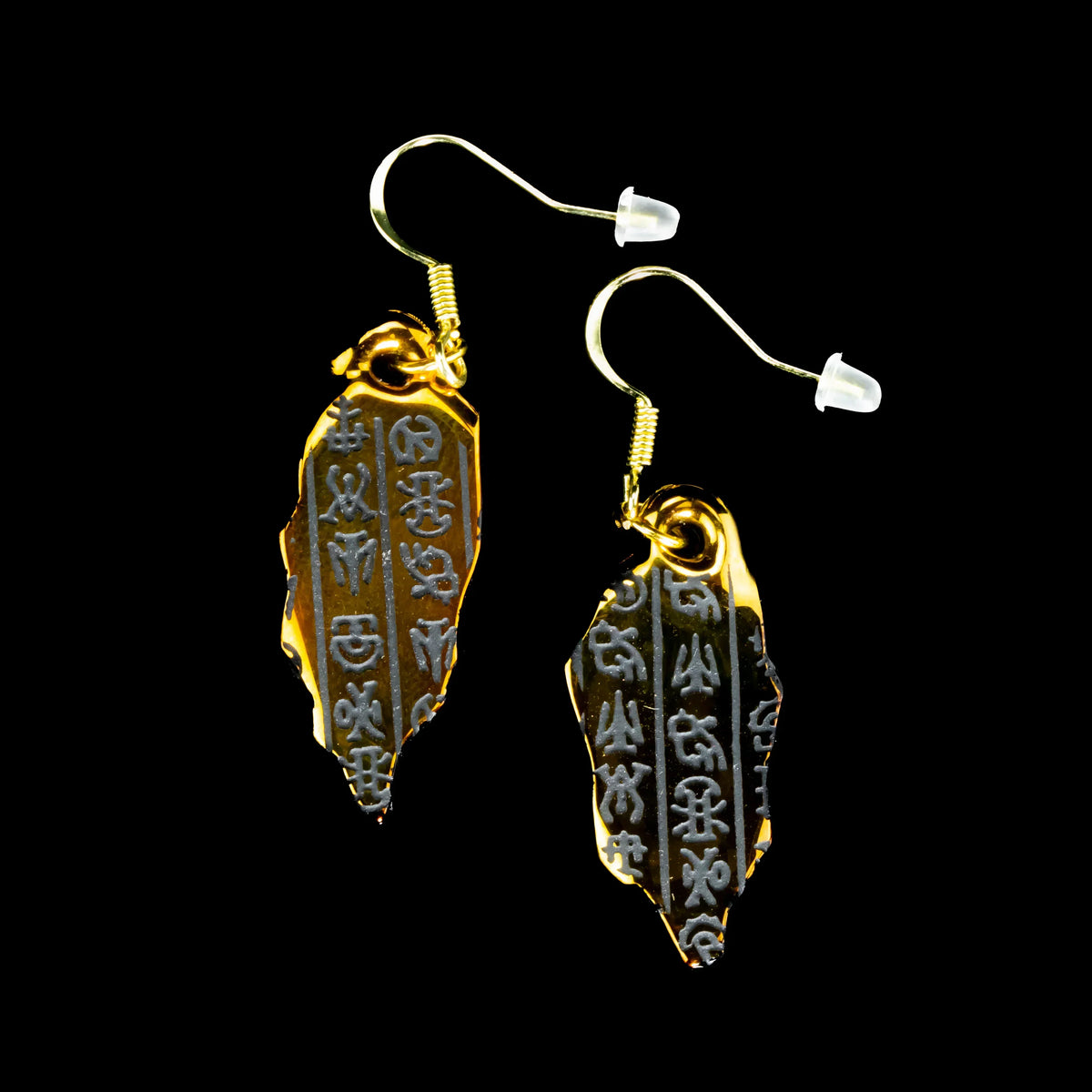 Gold artifact-inspired earrings with engraved symbols on black background