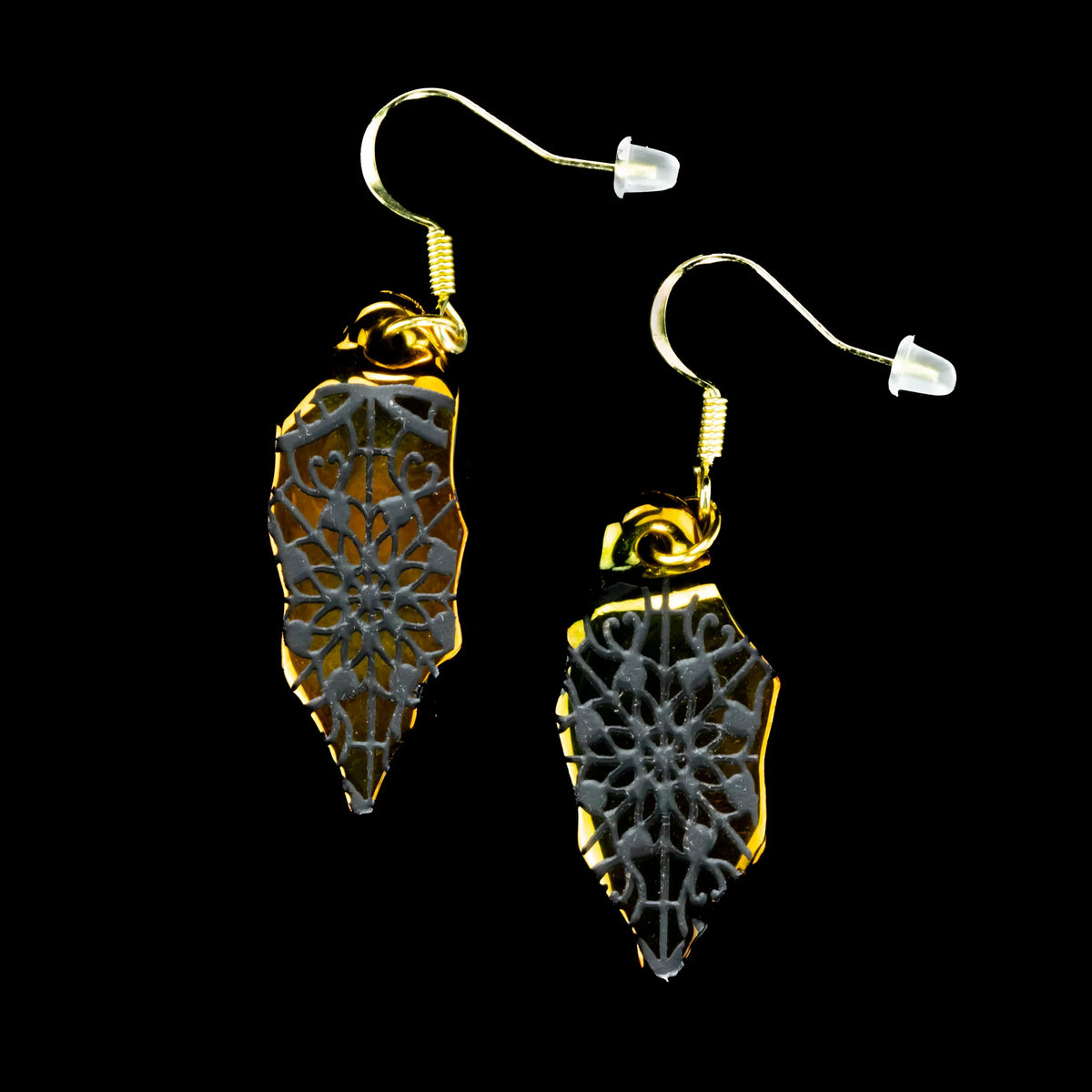 Gold and black artifact earrings with intricate stained glass pattern on a black background