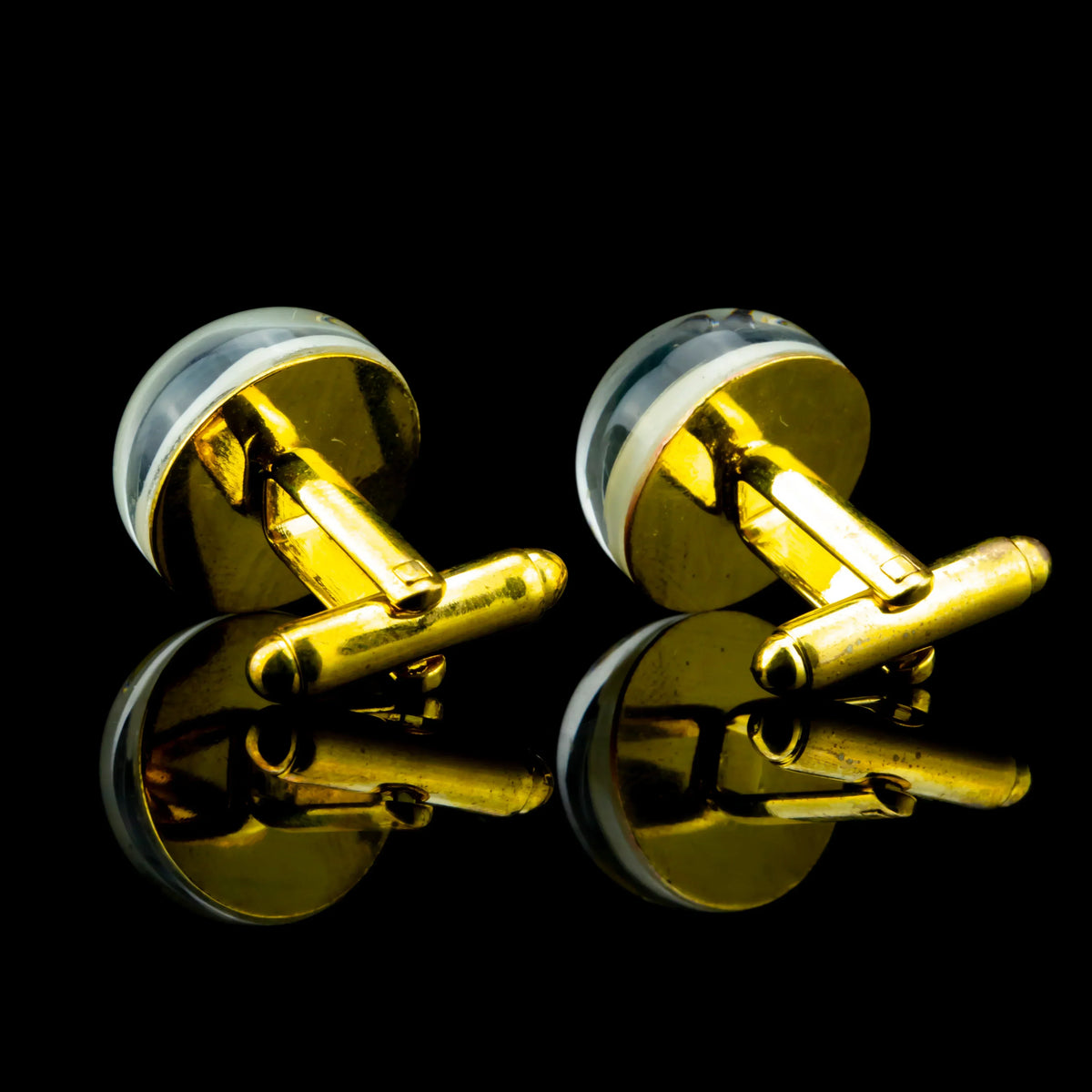 Gold and glass round cufflinks with clear tops on a black reflective surface