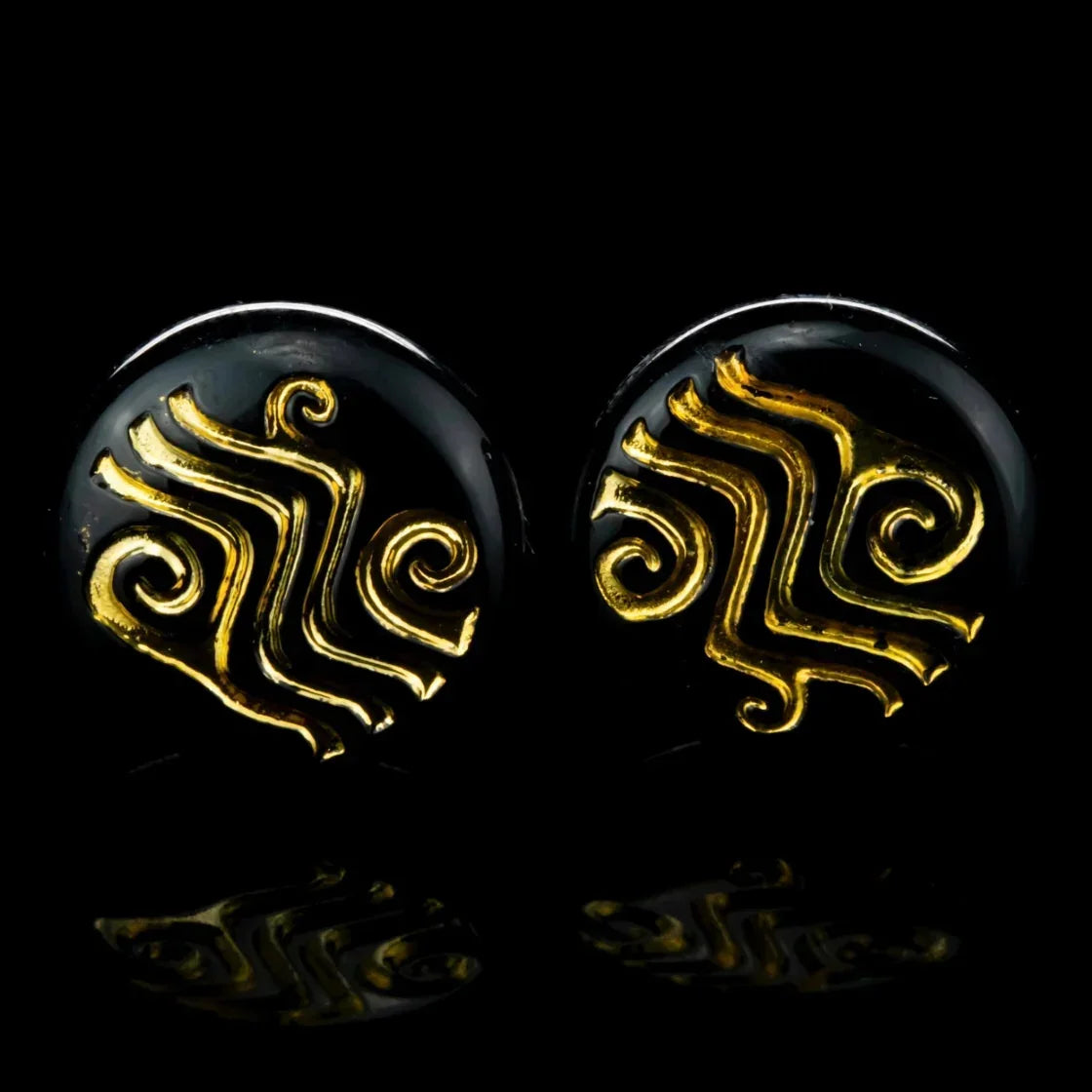 Black stud earrings with gold swirl designs on a dark background